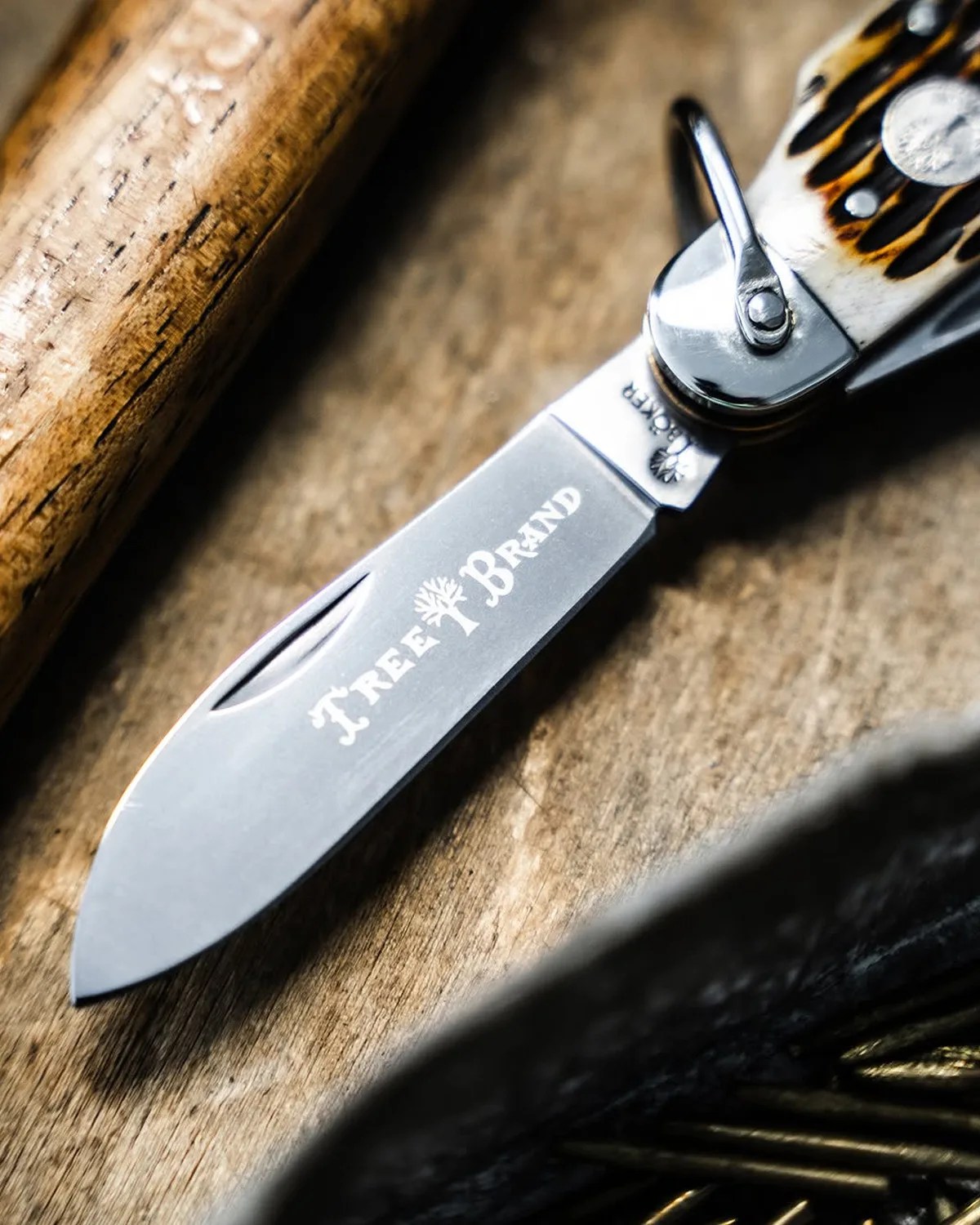 Close-up of a folding knife blade with "Tree Brand" engraved, featuring a patterned handle and wooden surface background.