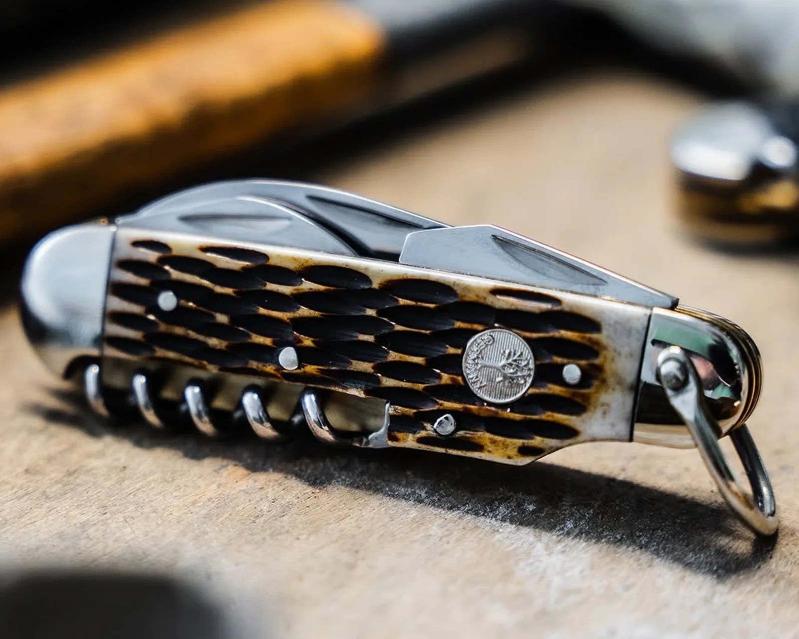 Close-up of a closed pocket knife with a textured brown and black handle and a metal corkscrew on a wooden surface.