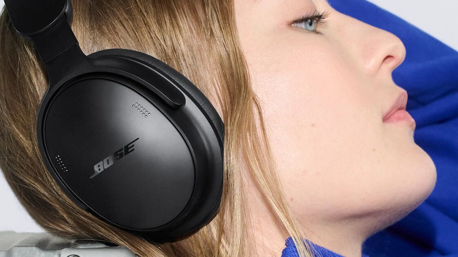 Black Bose over-ear headphones worn by a person with light brown hair and blue clothing.