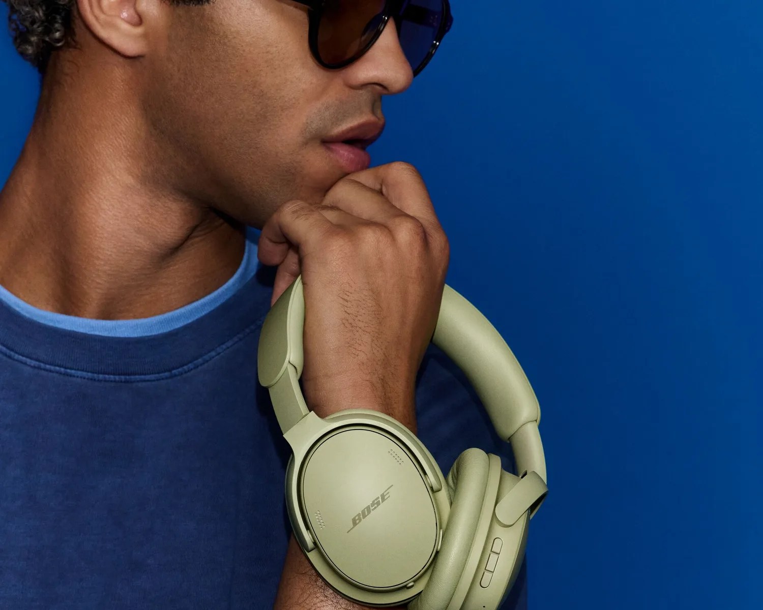 Person holding olive green Bose over-ear headphones against a blue background.