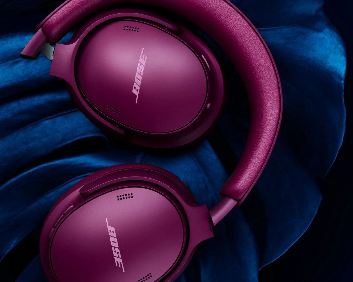 Purple Bose over-ear headphones resting on dark blue fabric.