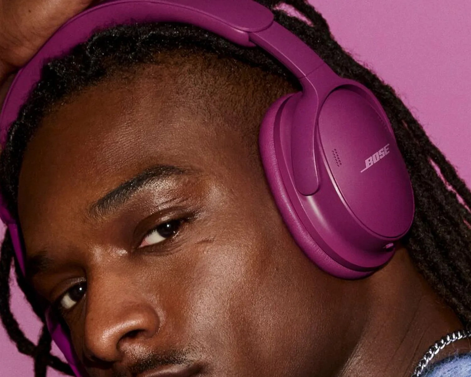 Close-up of a person wearing purple Bose over-ear headphones against a purple background.