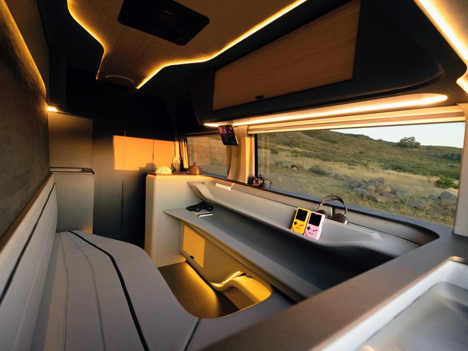 Interior of a modern camper van with gray seating, ambient lighting, and a large window showing a grassy landscape.