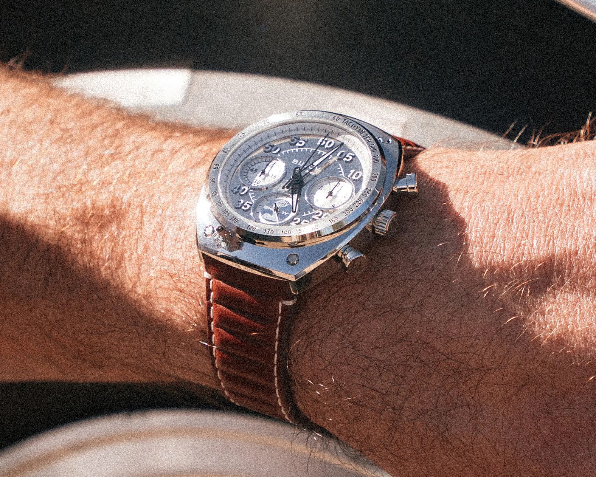 Silver chronograph wristwatch with black and white dial and brown leather strap on a wrist.
