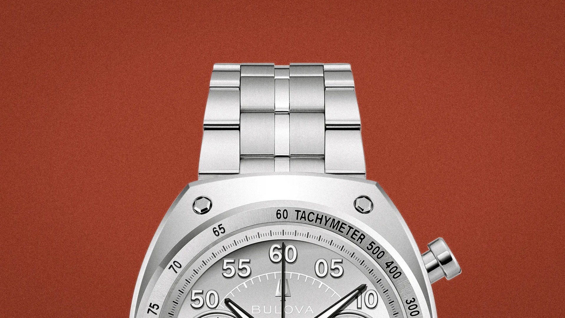 Close-up of a silver metal watch band and part of a silver chronograph watch face with tachymeter markings on a reddish-brown background.