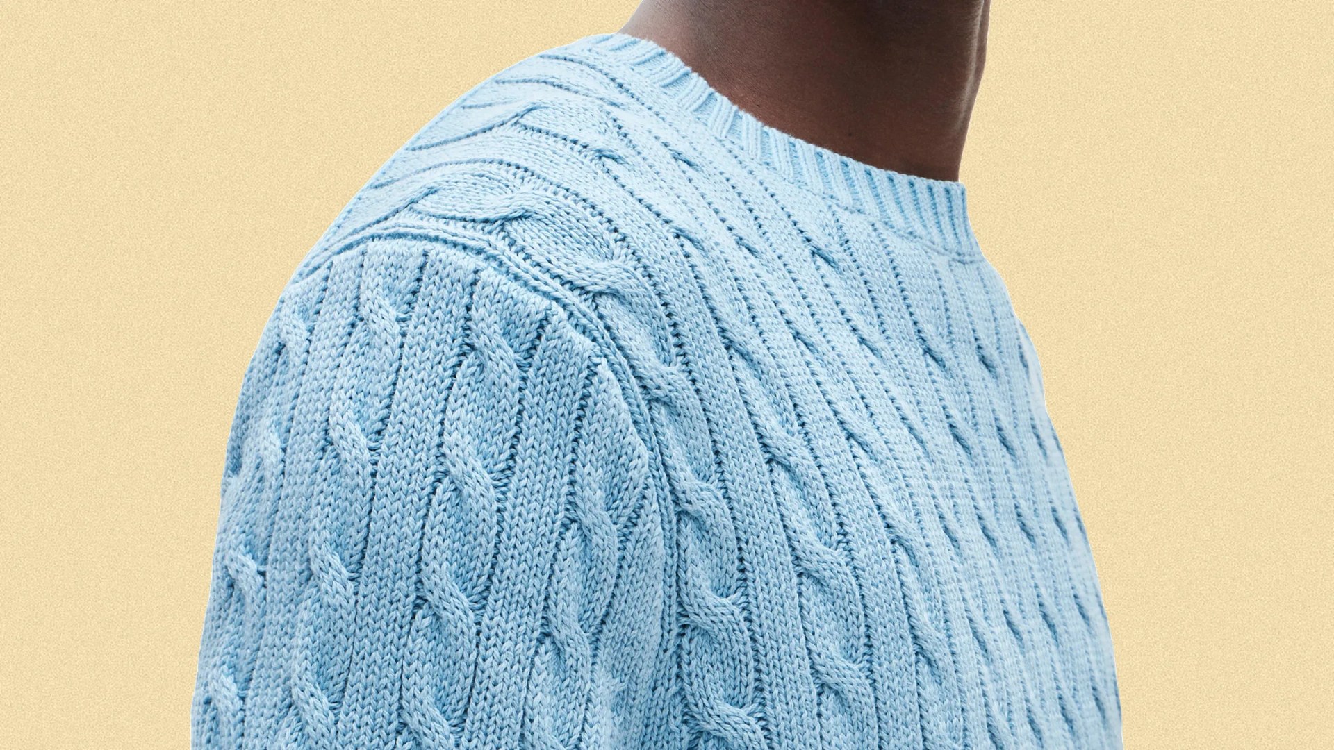 Light blue cable-knit sweater with ribbed crew neckline worn by a person against a beige background.