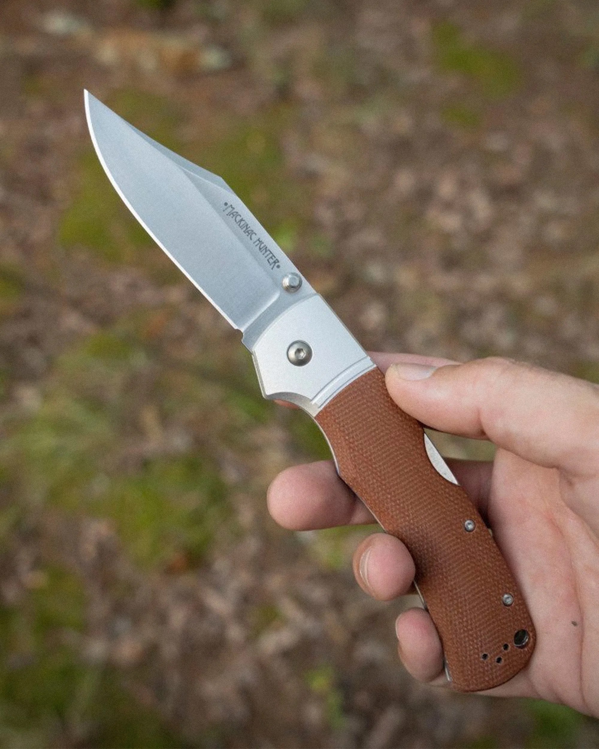 Hand holding a folding knife with a silver blade and brown textured handle.