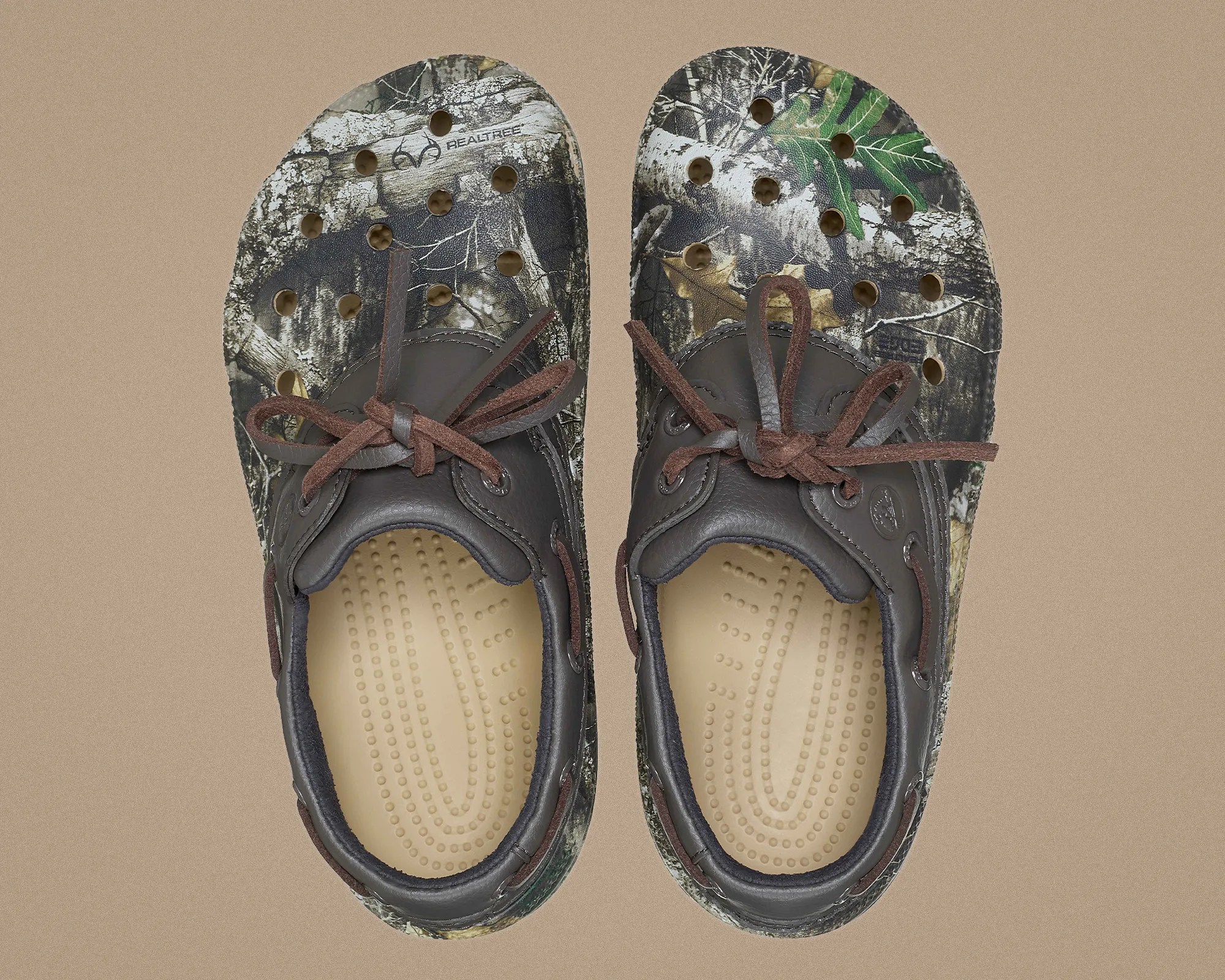 Pair of Realtree camouflage slip-on shoes with brown laces and beige textured insoles on a tan background.