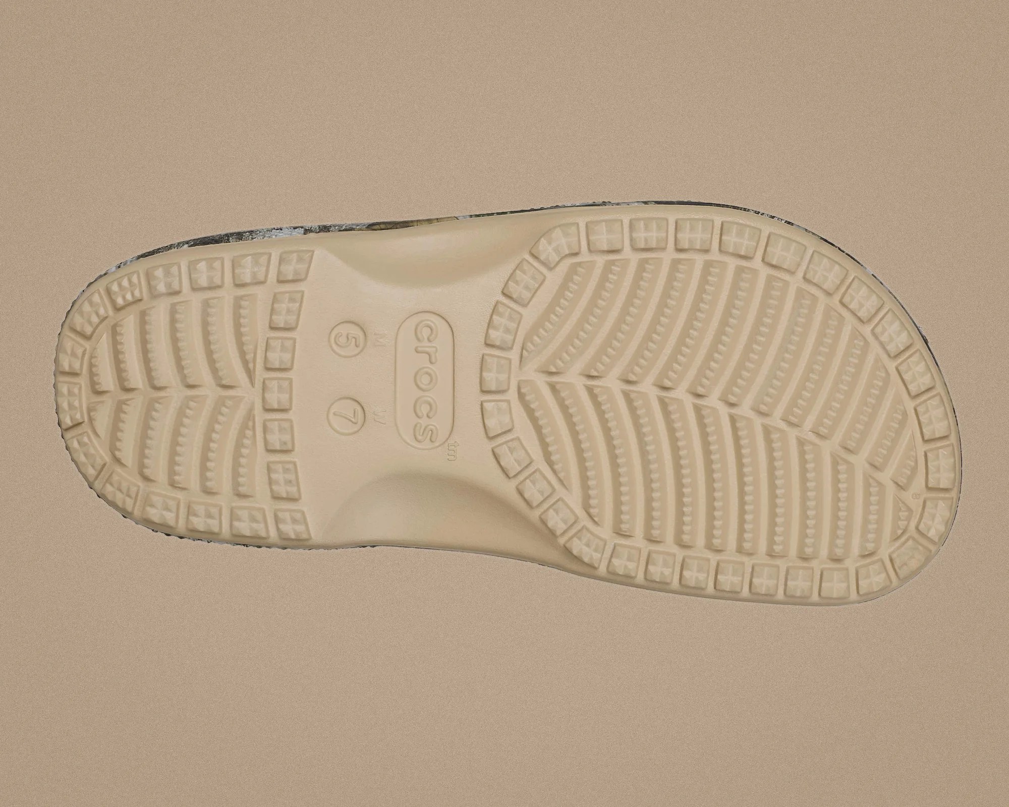 Beige Crocs shoe sole with textured tread pattern on a tan background.
