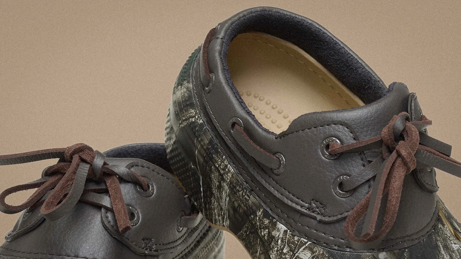 Close-up of dark gray leather boat shoes with brown suede laces and camouflage-patterned rubber soles.