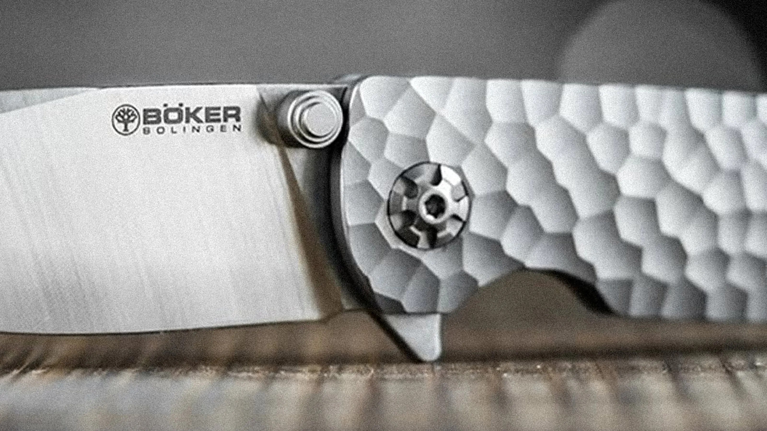 Close-up of a B&ouml;ker Solingen folding knife blade and textured metal handle with a circular pivot screw.