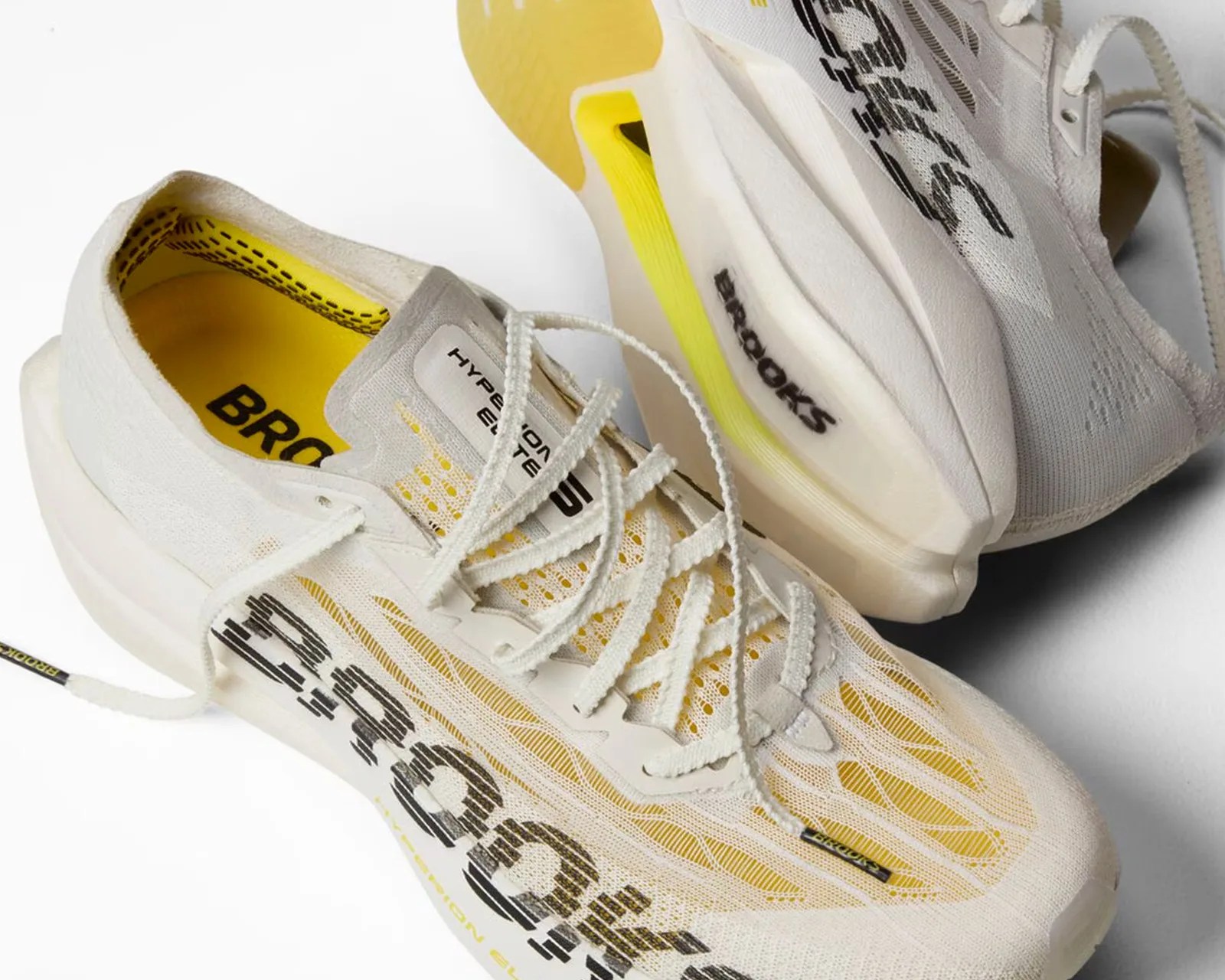 Pair of white Brooks Hyperion Elite running shoes with yellow insoles and black branding.