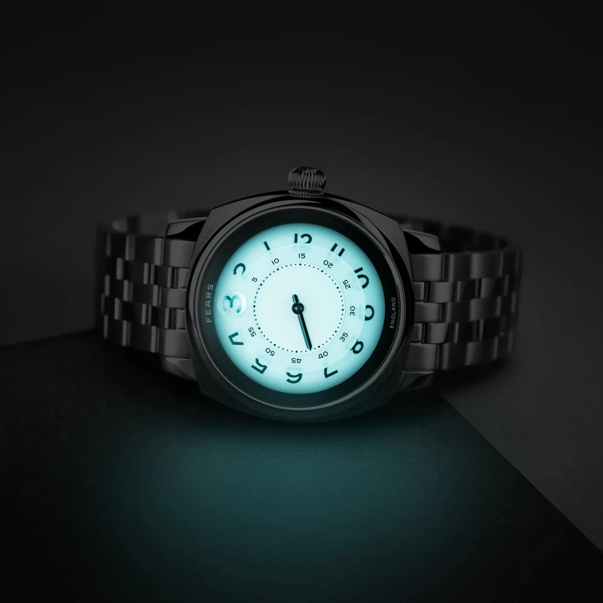 Metal wristwatch with glowing blue dial and Arabic numerals on a dark surface.