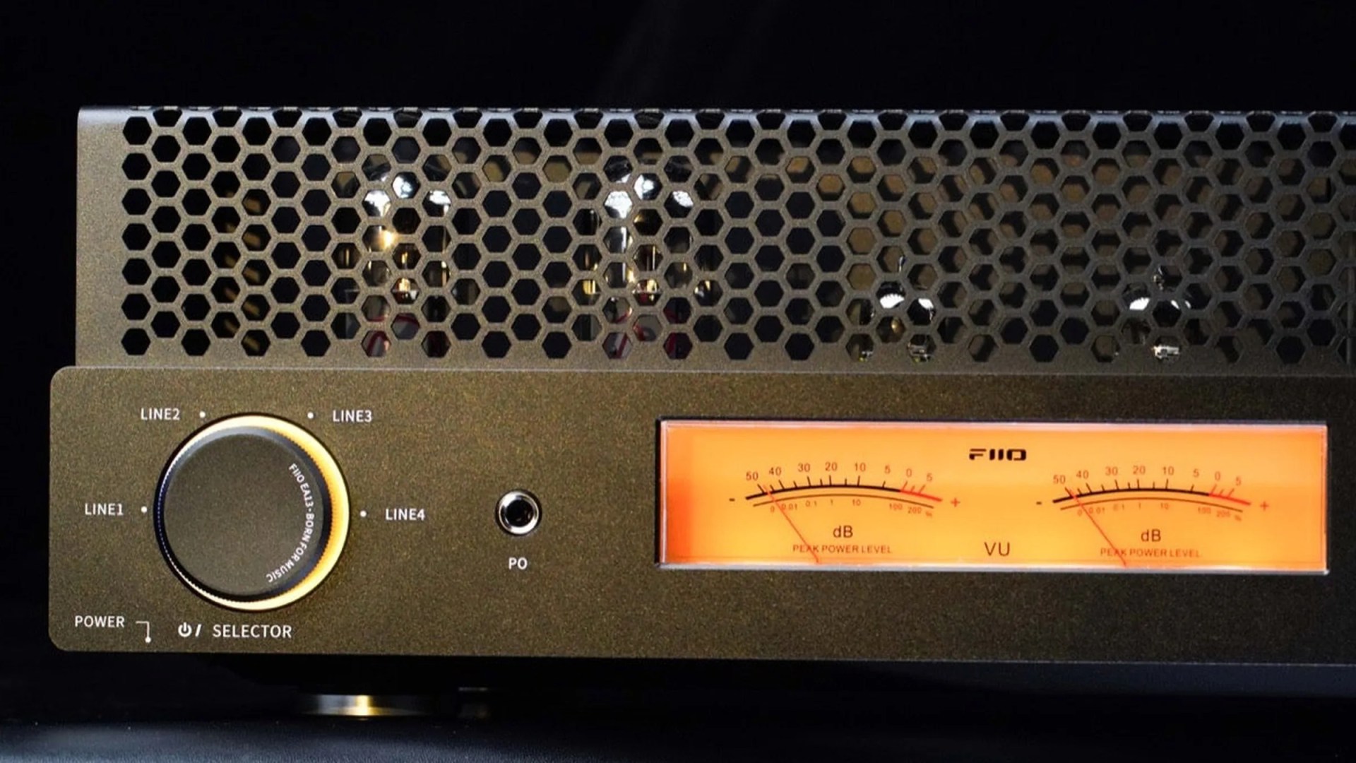 Black audio amplifier with honeycomb metal grille, large selector knob, and dual orange VU meters.