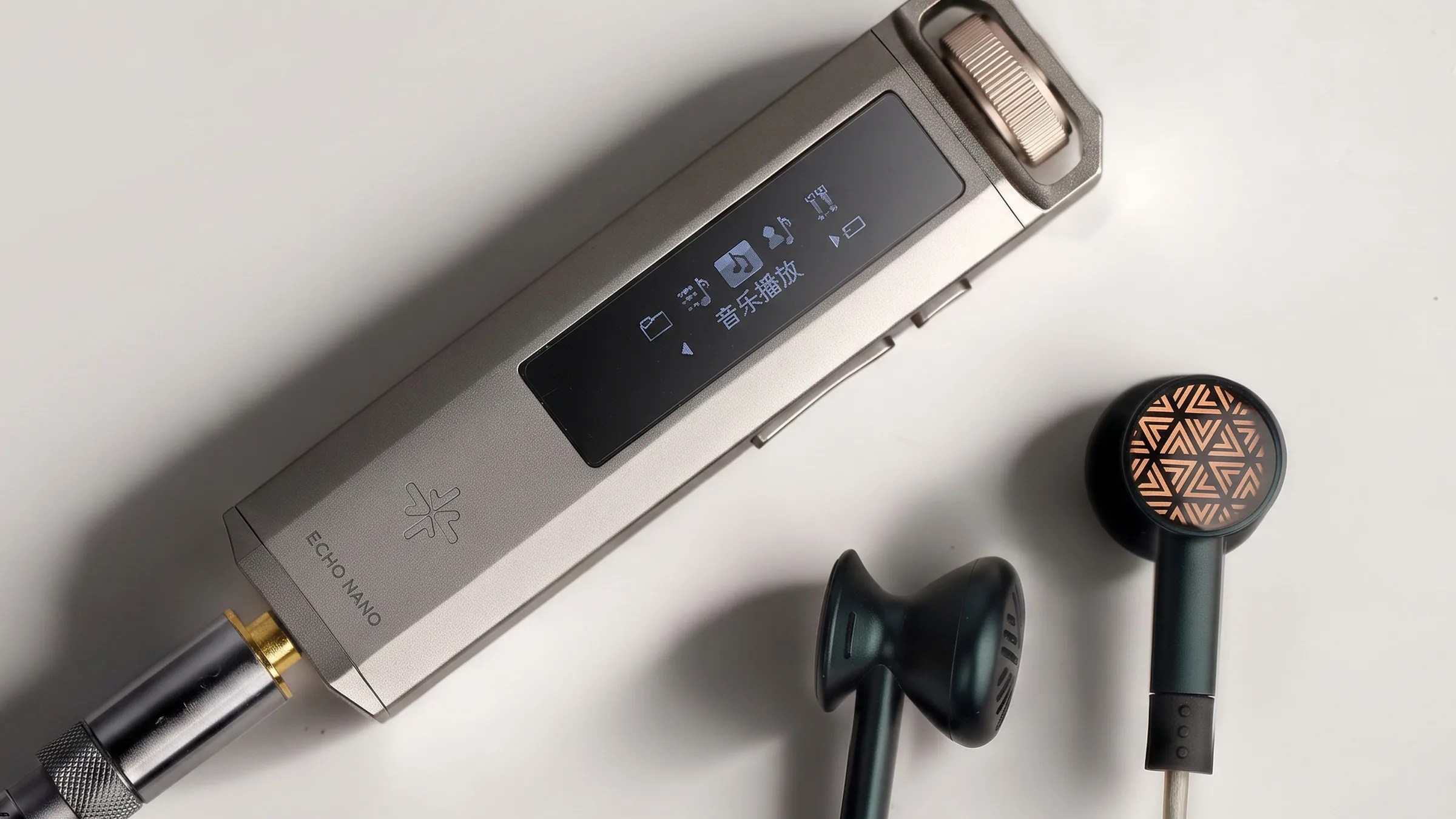Silver Echo Nano audio device with black wired earbuds featuring a copper geometric pattern on a white surface.