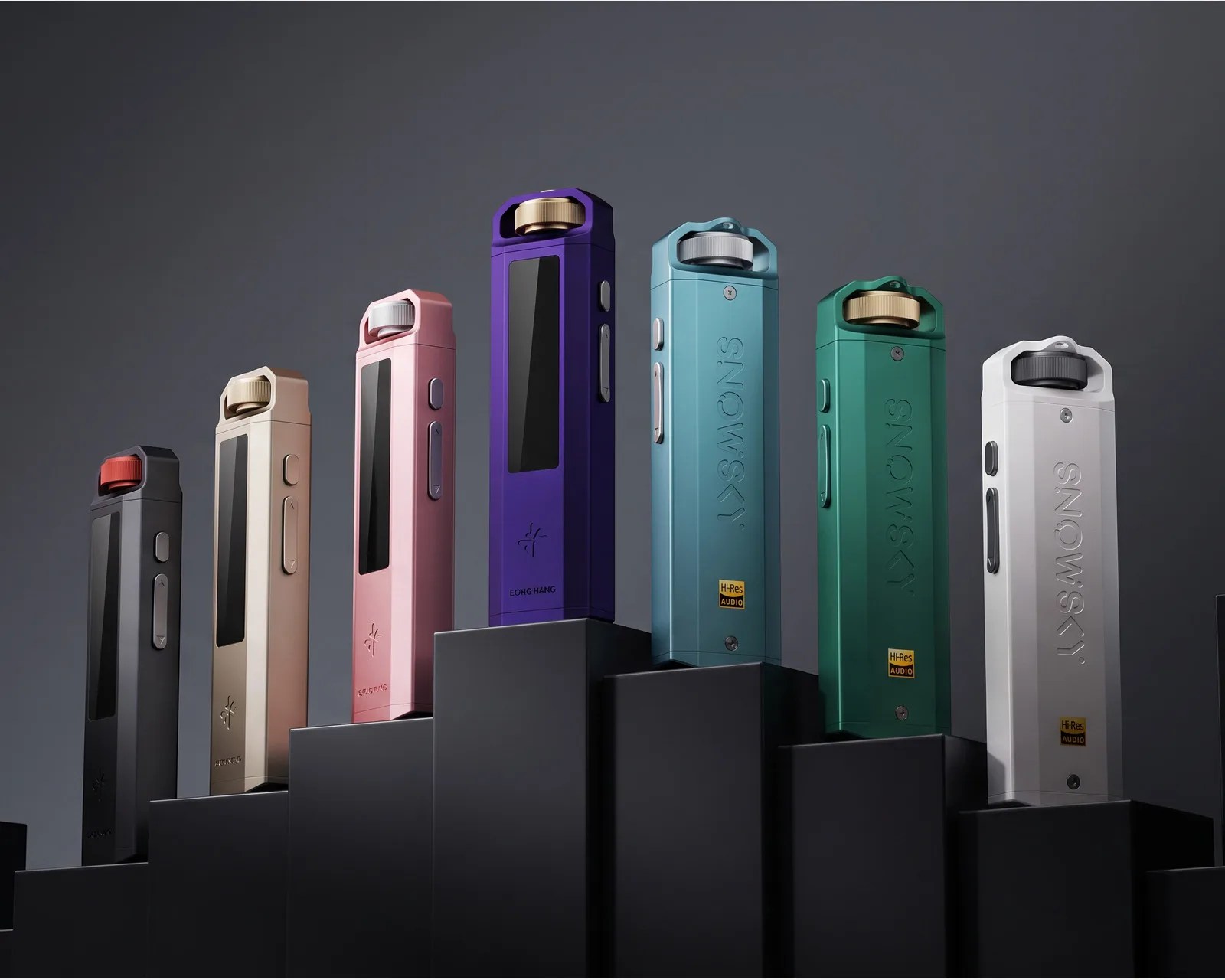 Seven colorful rectangular electronic devices with screens and rotary knobs on top, displayed on black stepped platforms against a gray background.