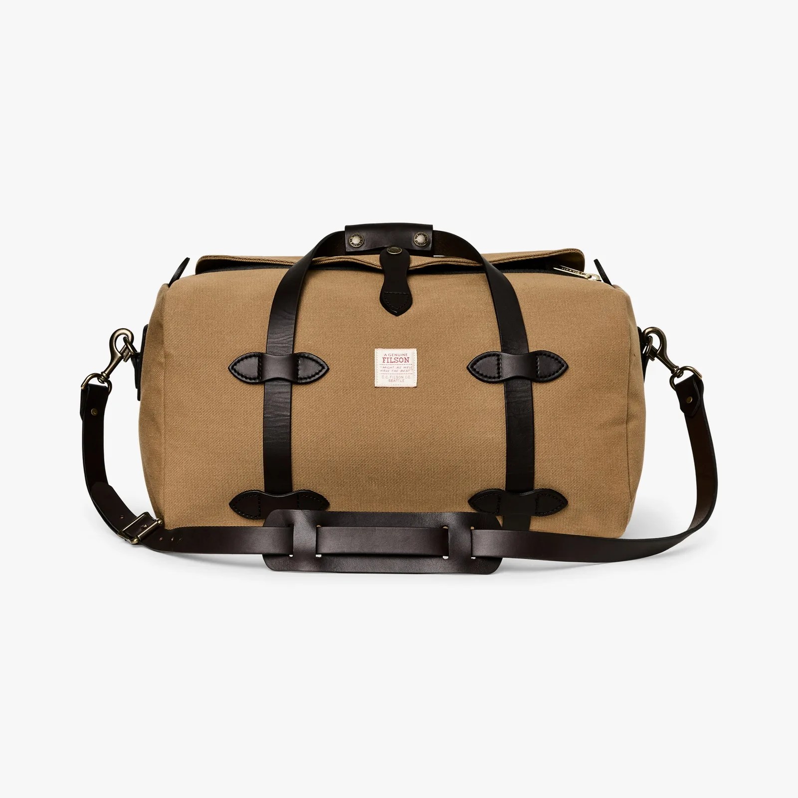 Tan canvas duffel bag with black leather straps and shoulder pad, featuring a small white label on the front.
