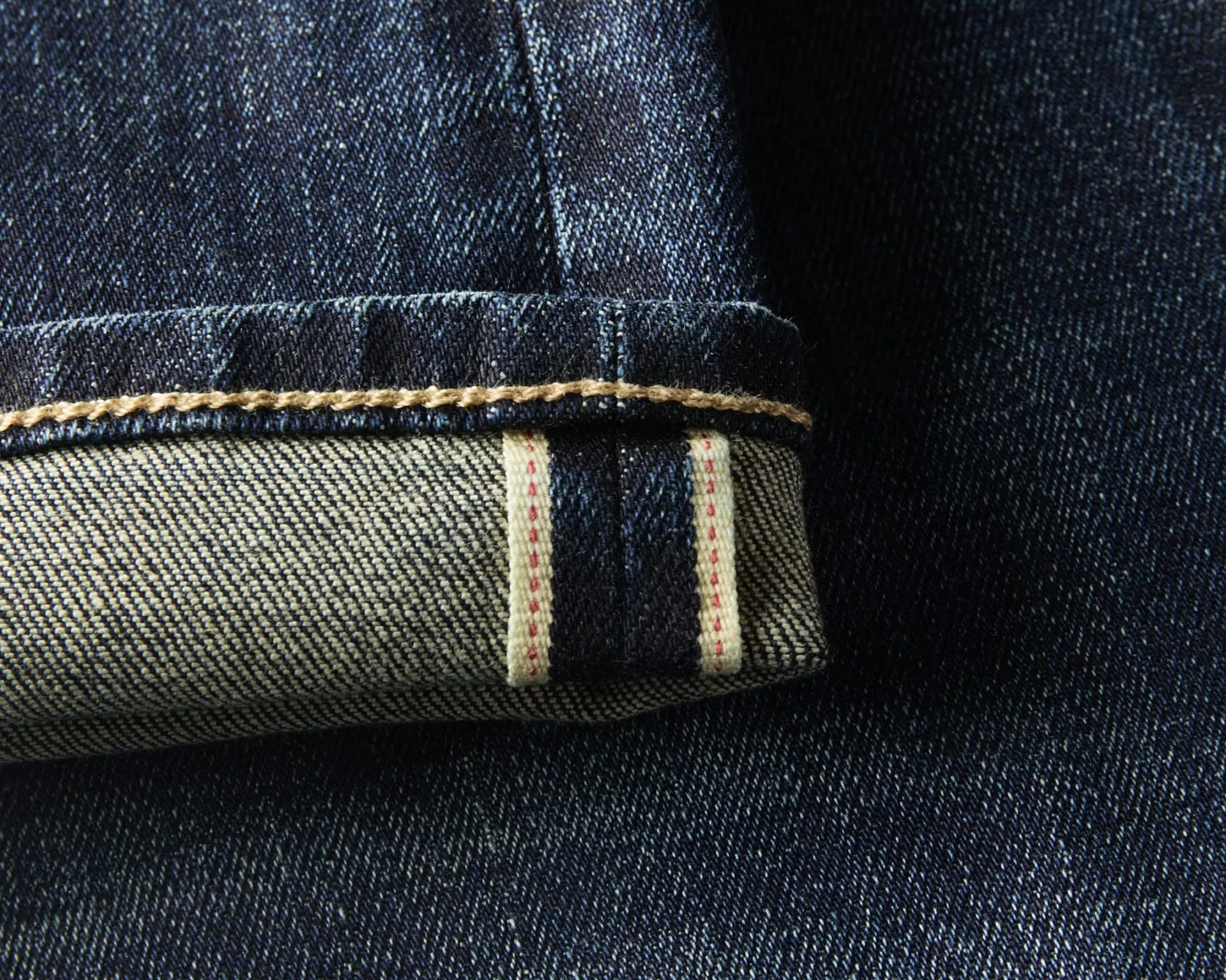 Close-up of dark blue denim jeans cuff with visible selvedge edge and beige stitching.
