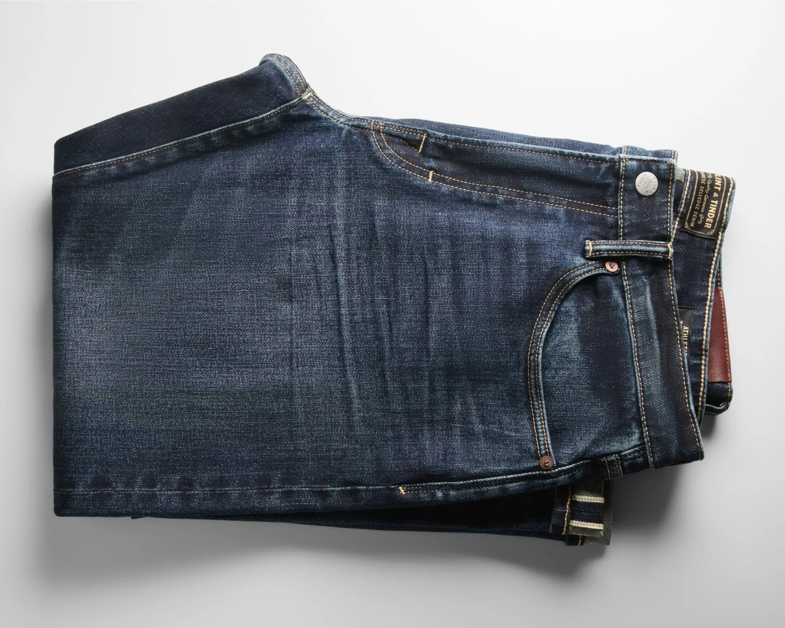 Folded dark blue denim jeans with visible stitching and a leather patch on the waistband.
