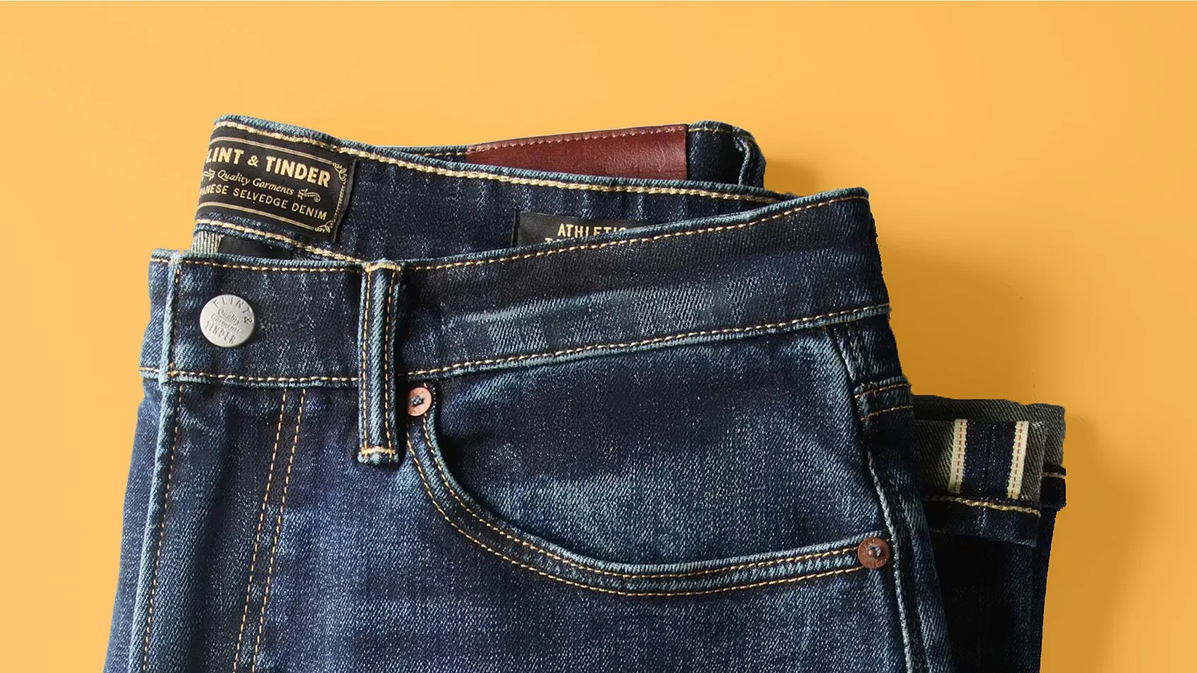 Folded dark blue Japanese selvedge denim jeans with visible brand label and button on a yellow background.