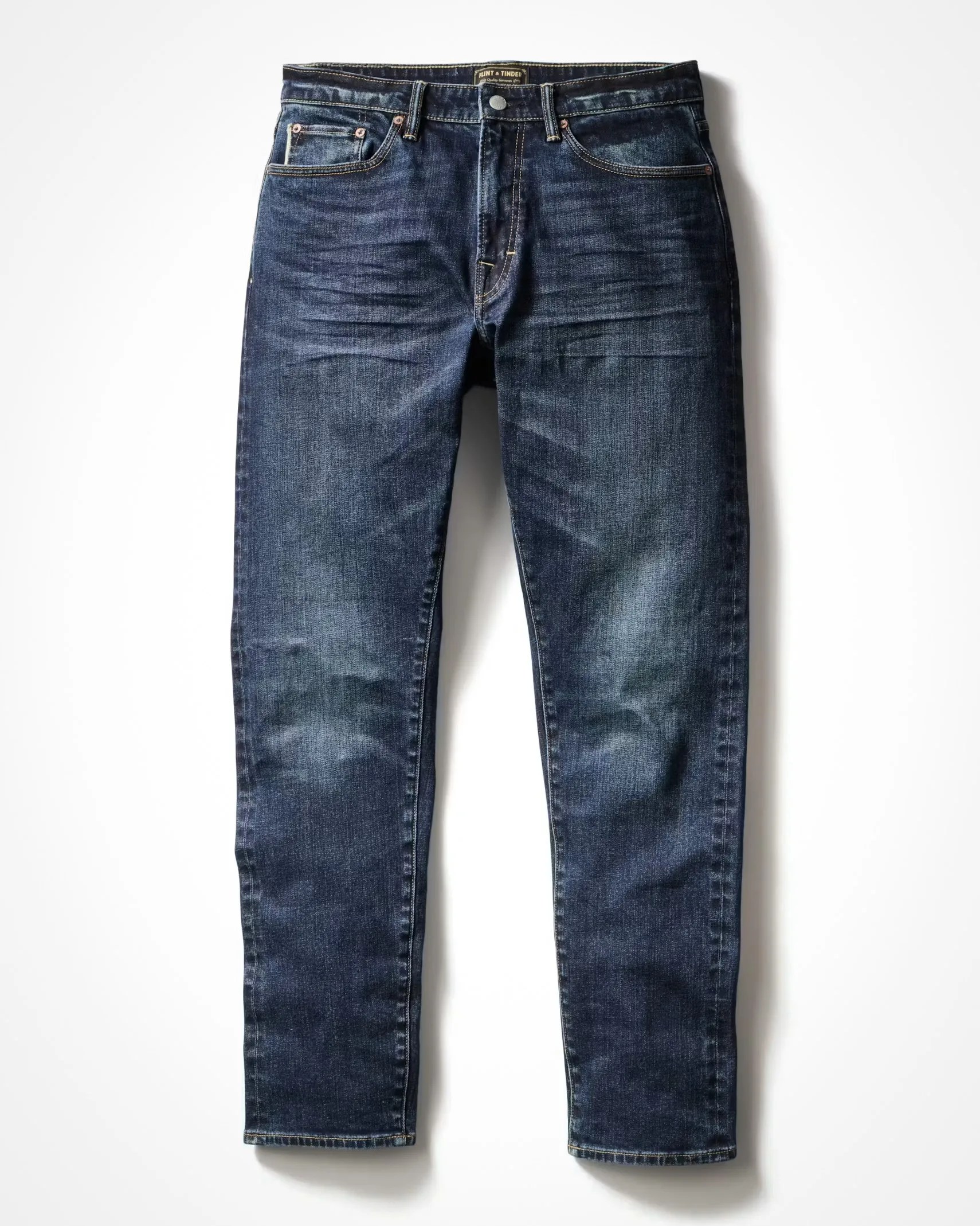 Dark blue denim jeans with slight fading and whiskering details, laid flat on a white surface.