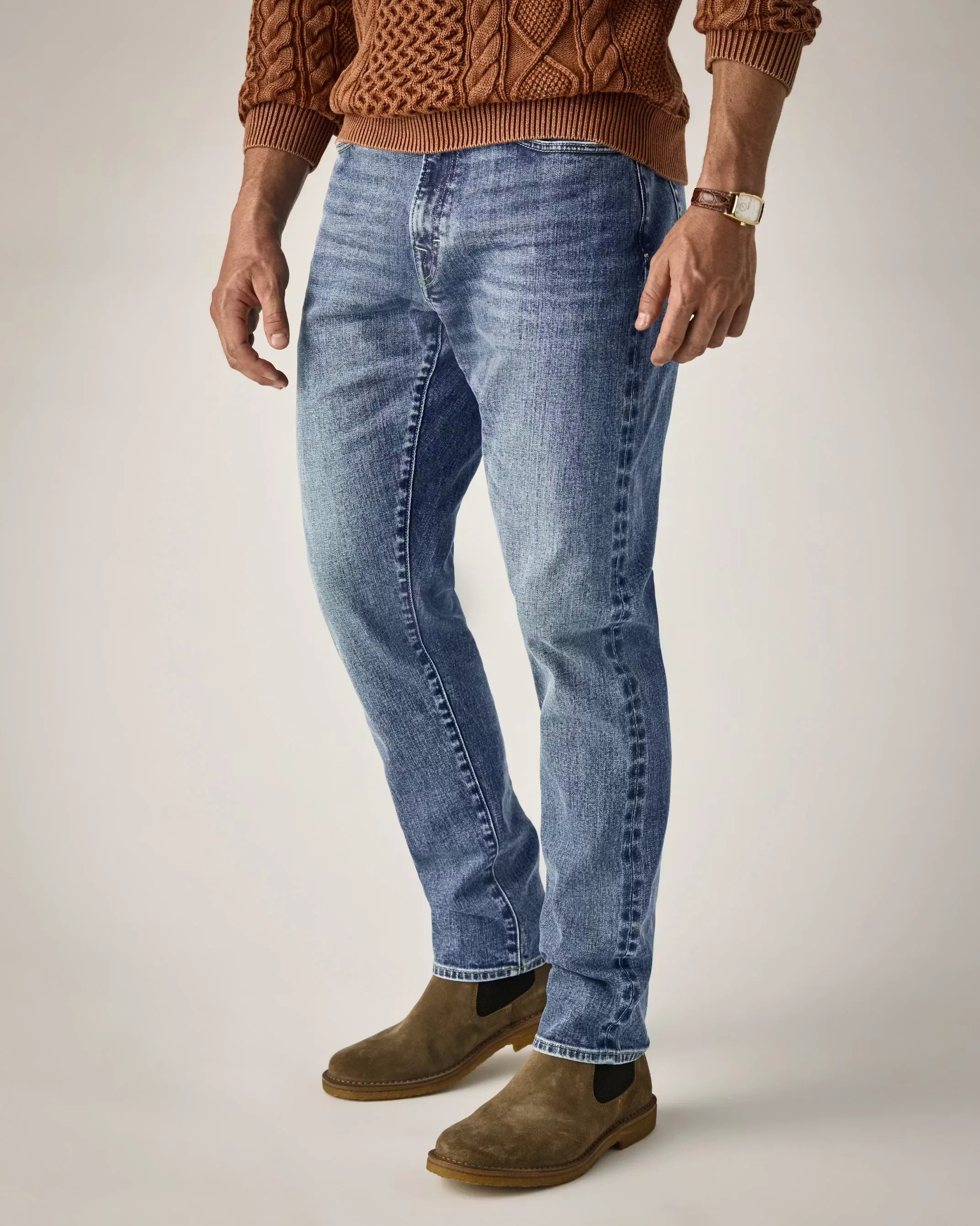 Light blue faded jeans paired with brown suede Chelsea boots and a brown cable-knit sweater.