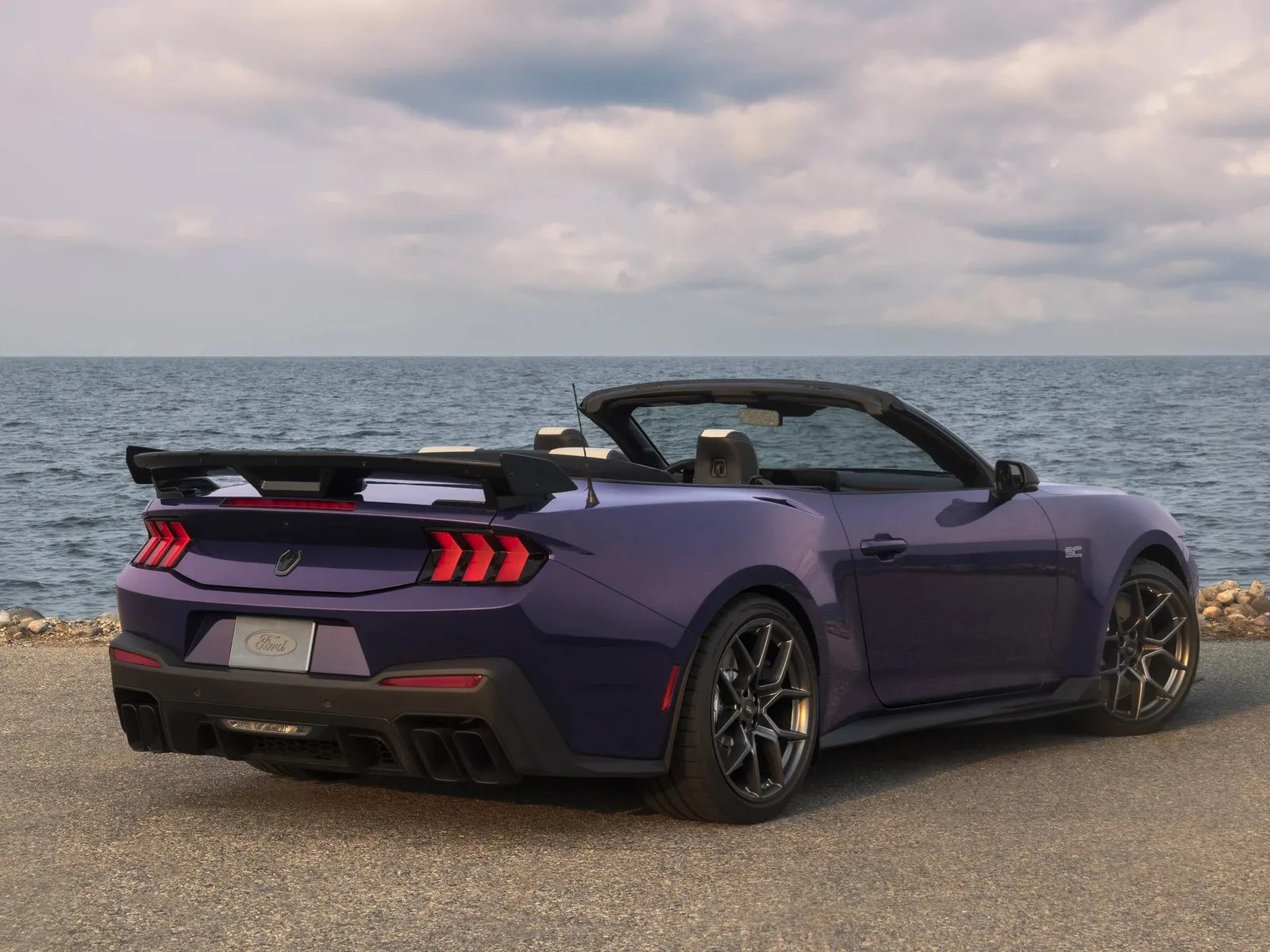 Purple Ford convertible sports car with black rear spoiler parked near the ocean.