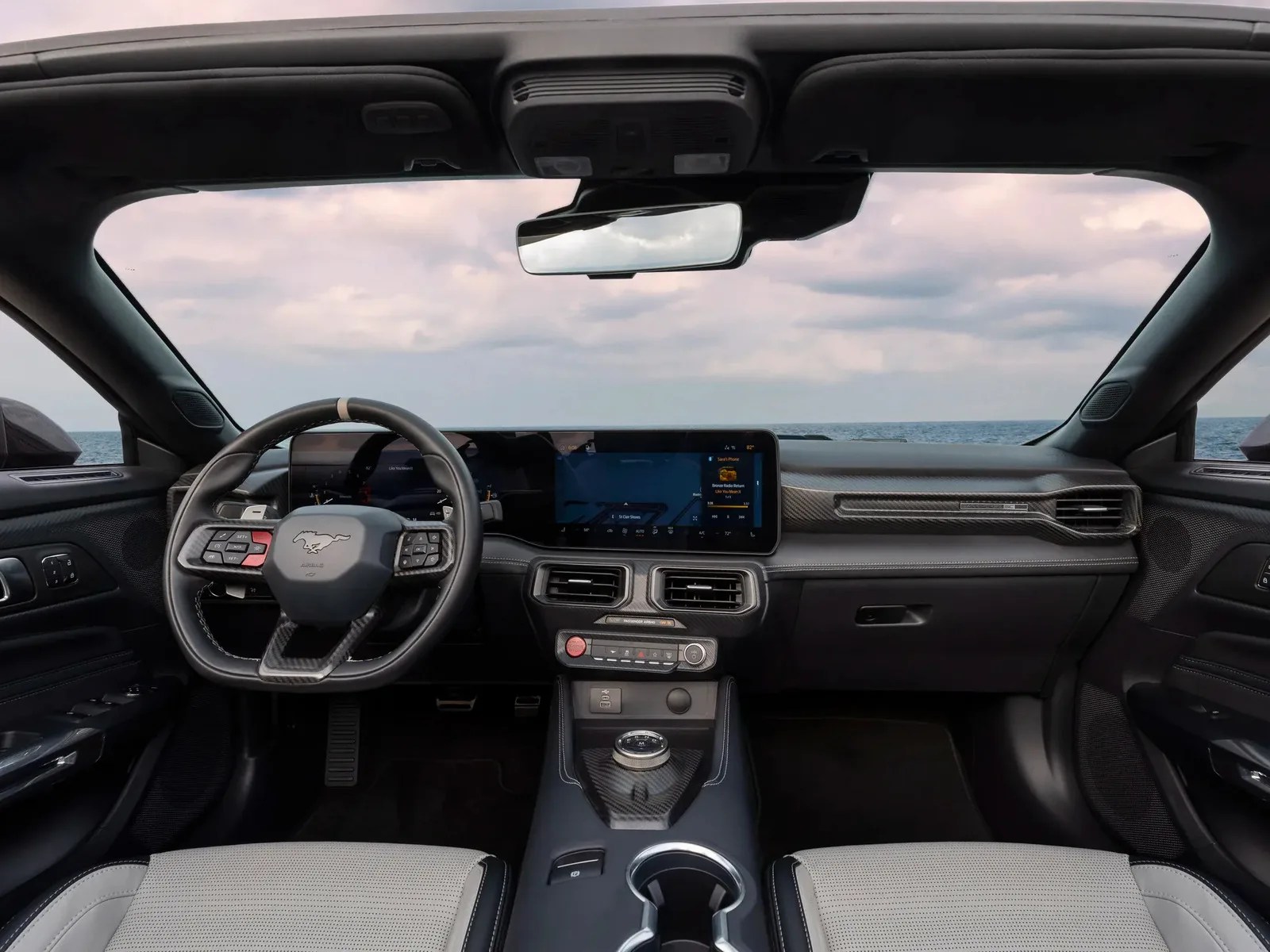 Interior of a Ford Mustang Mach-E with black and gray seats, digital dashboard, and carbon fiber accents.