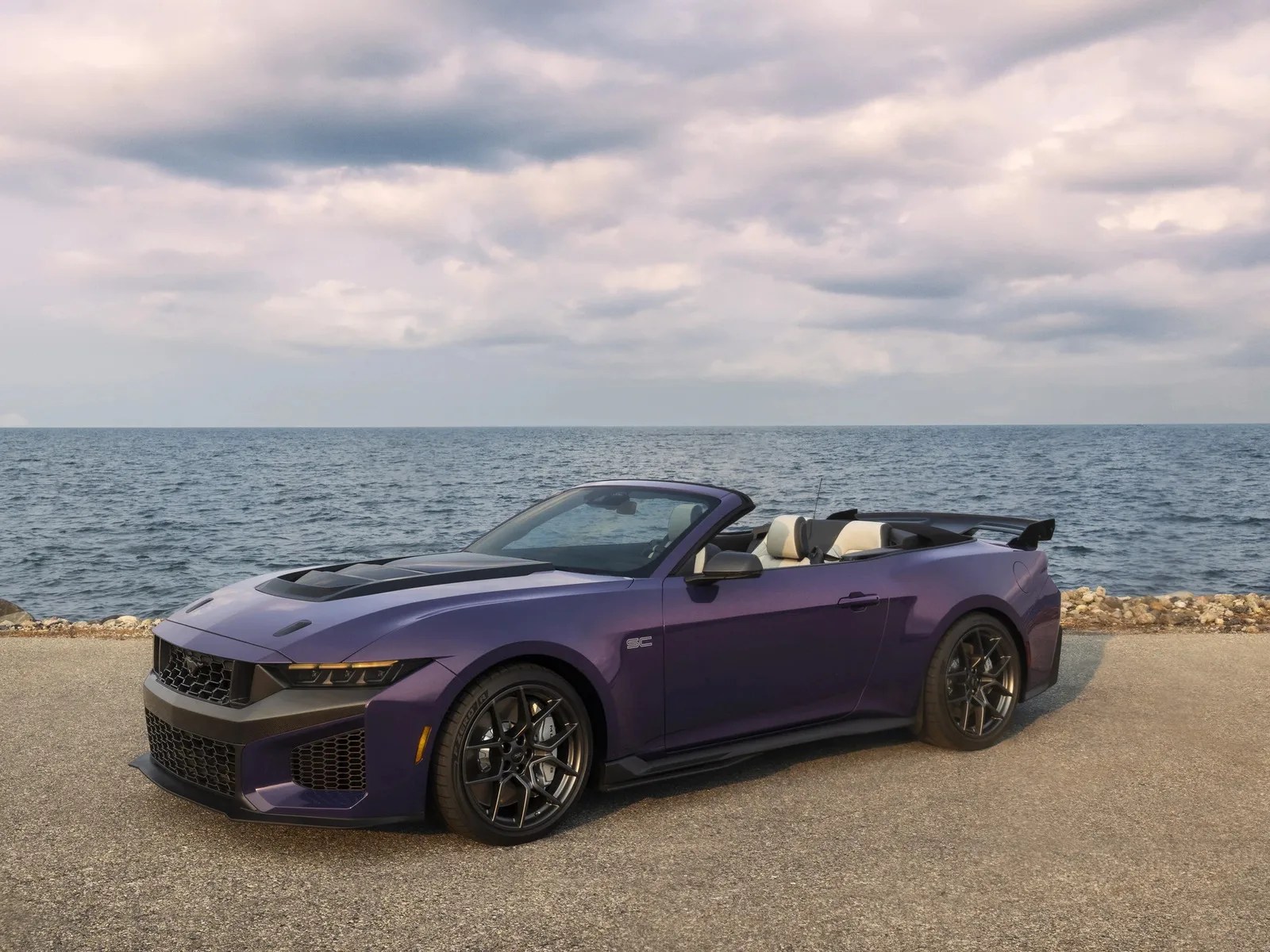 Purple convertible sports car with black hood vents and black wheels parked by the ocean.
