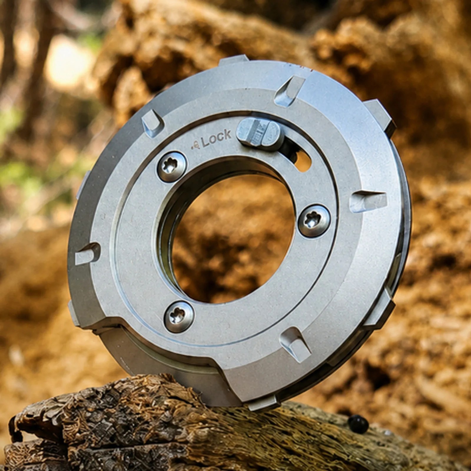 Silver metal circular mechanical part with screws and a lock switch resting on textured wood.