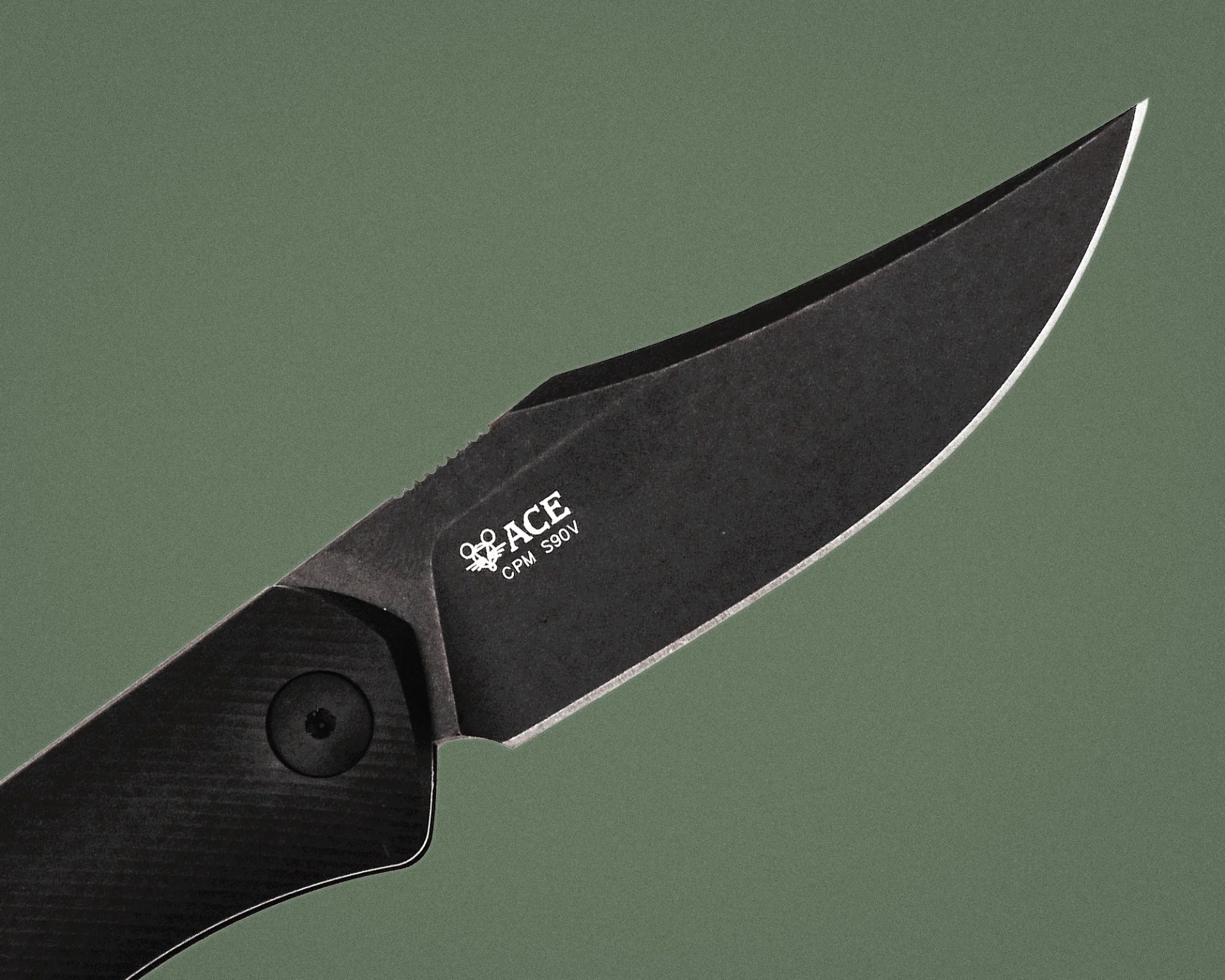 Black folding knife blade with "ACE CPM S90V" text and black textured handle against a green background.