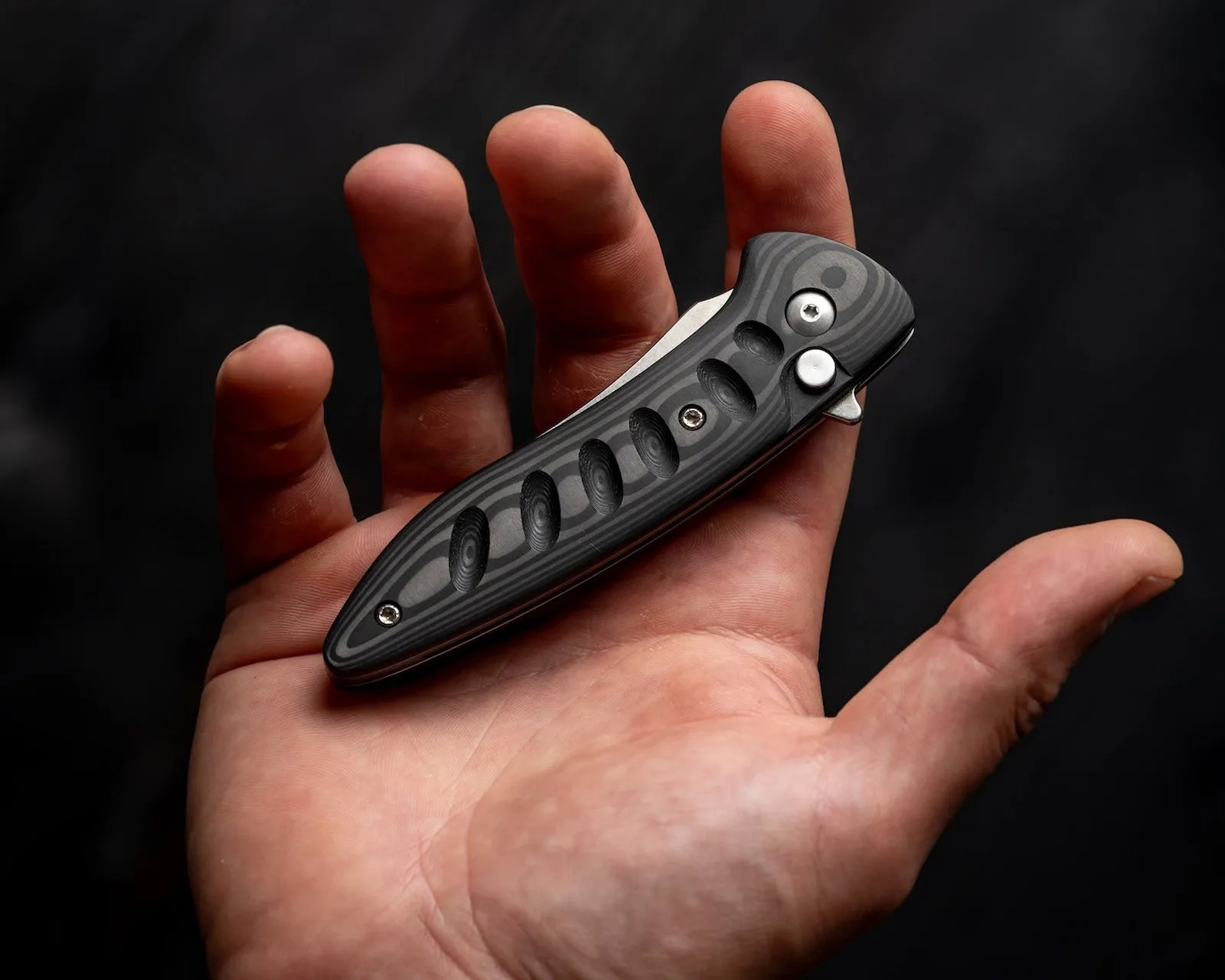 Hand holding a closed black folding knife with a textured handle and metal screws.