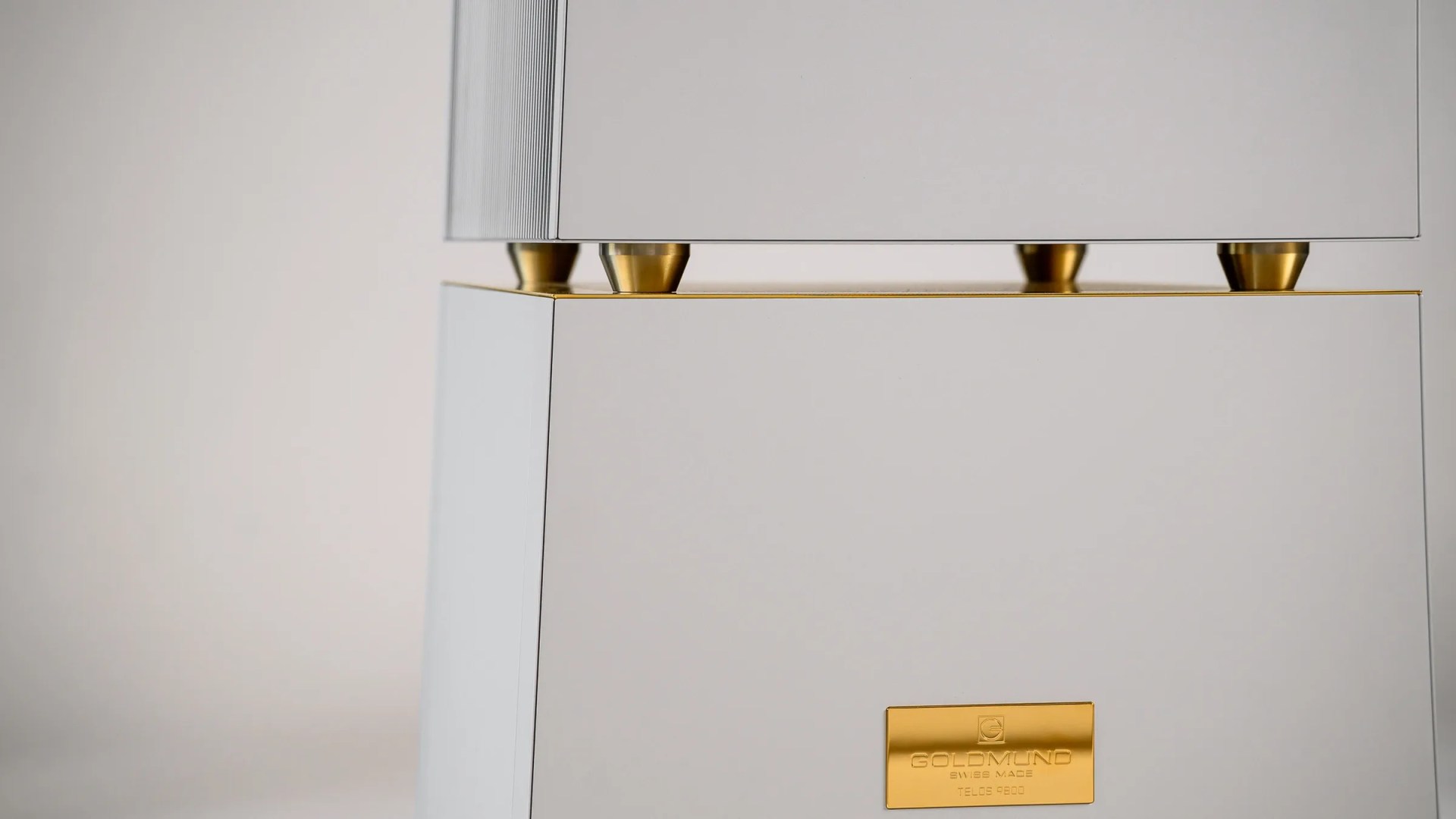 Close-up of a white Goldmund Telos 9800 speaker with gold accents and a gold logo plate.