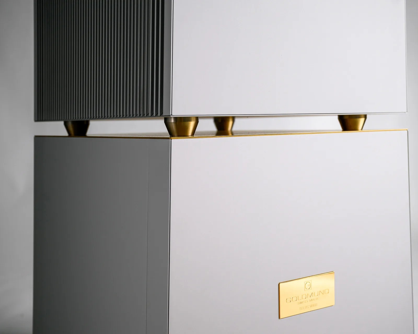 White and black rectangular speaker with gold accents and a gold label reading "Goldmund Swiss Made Relogium.