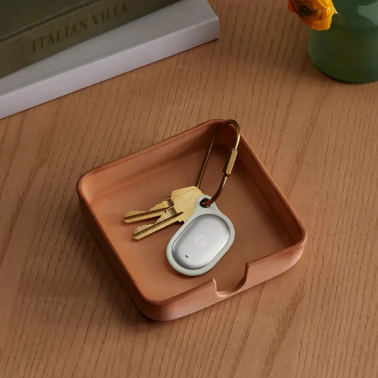 White Google Pixel key finder attached to brass keyring with two keys in a small wooden tray on a wood table.