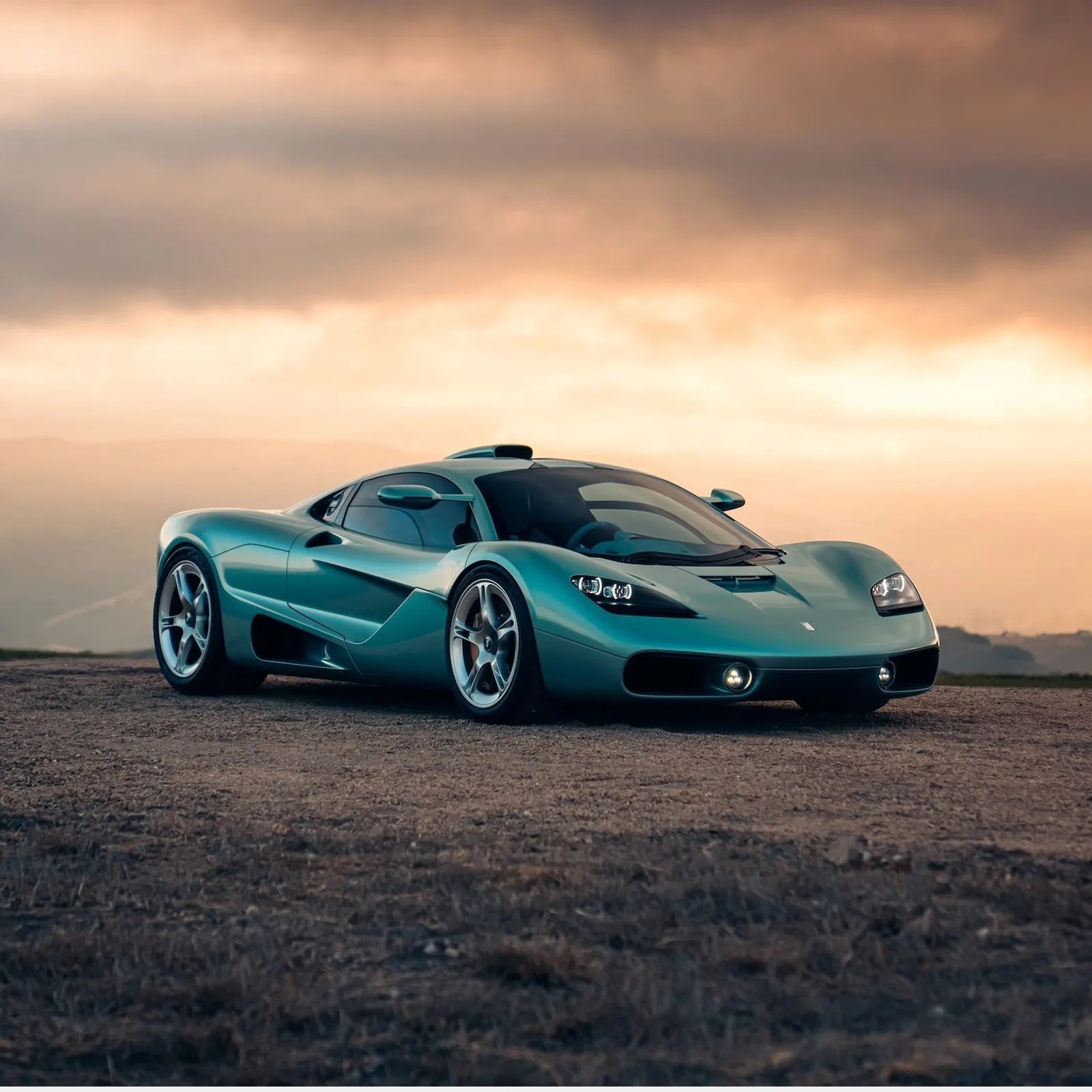 Teal metallic sports car with sleek aerodynamic design parked on a dirt surface under a cloudy sky.