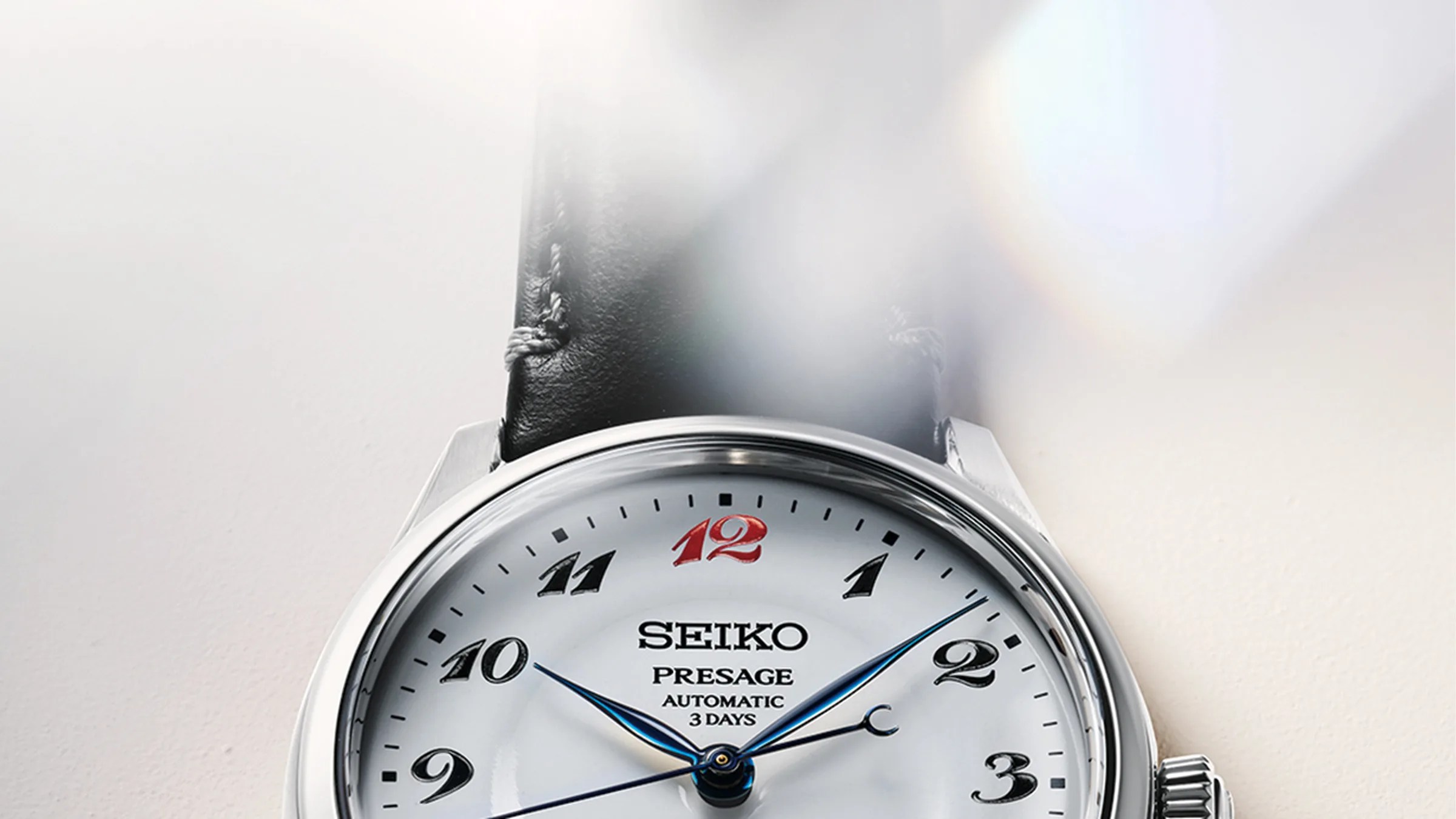 Close-up of a Seiko Presage automatic watch with a white dial, black leather strap, and blue hands.