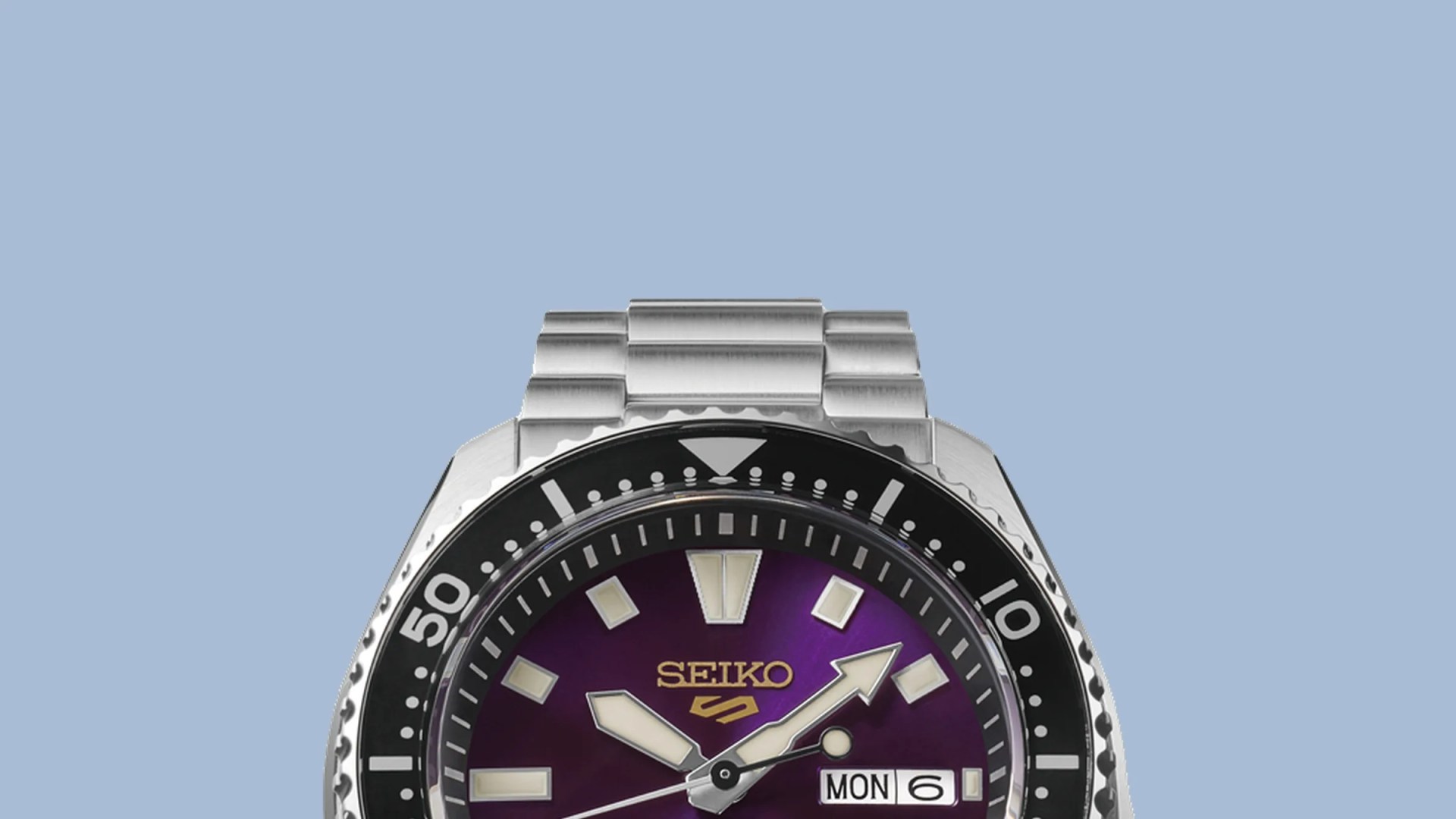 Close-up of a Seiko watch with a purple dial, silver hands, black bezel, and stainless steel bracelet.