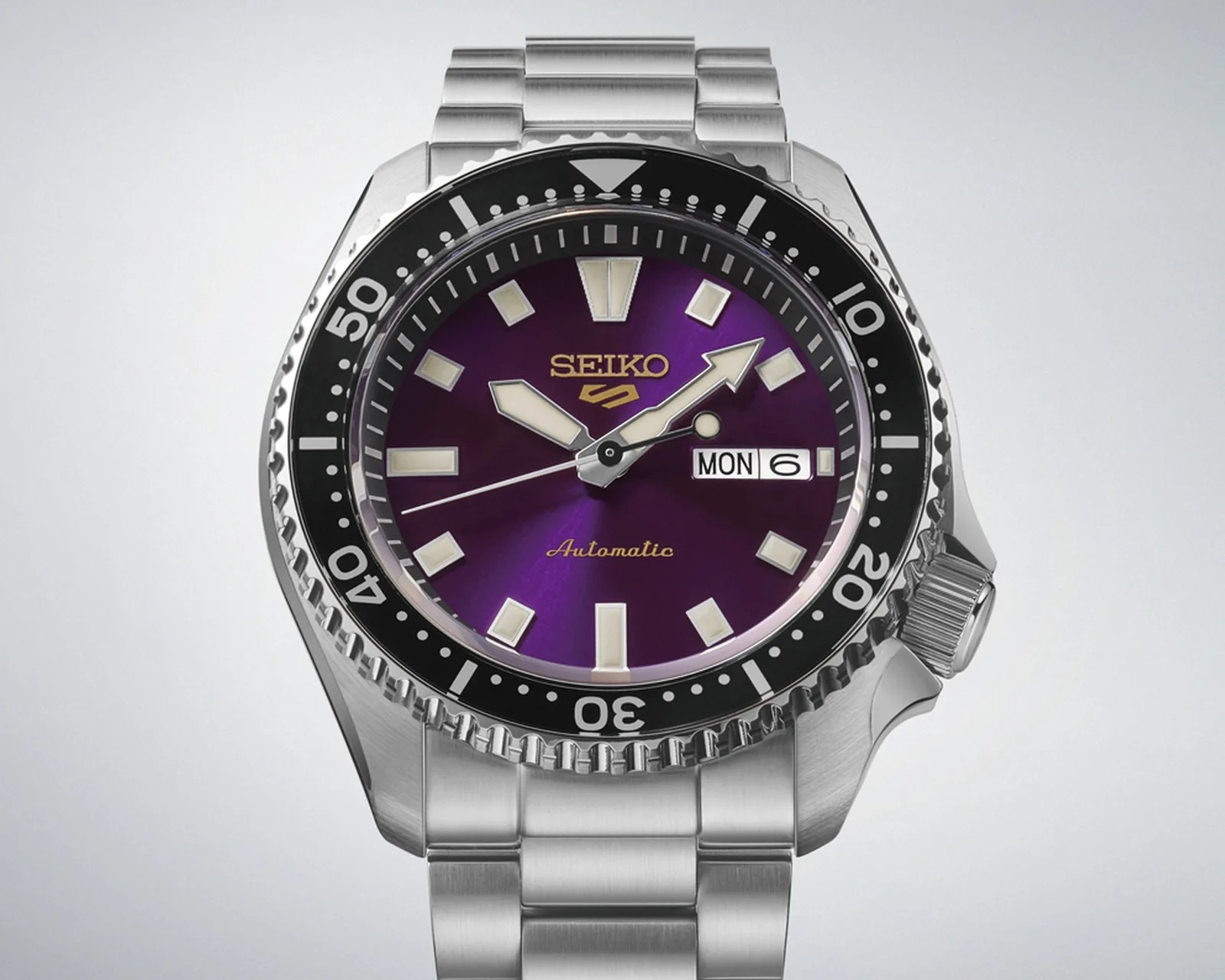 Seiko stainless steel wristwatch with purple dial, luminous markers, black bezel, and day-date display.