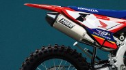 Rear section of a red, white, and blue Honda dirt bike with HGS exhaust system and knobby rear tire.