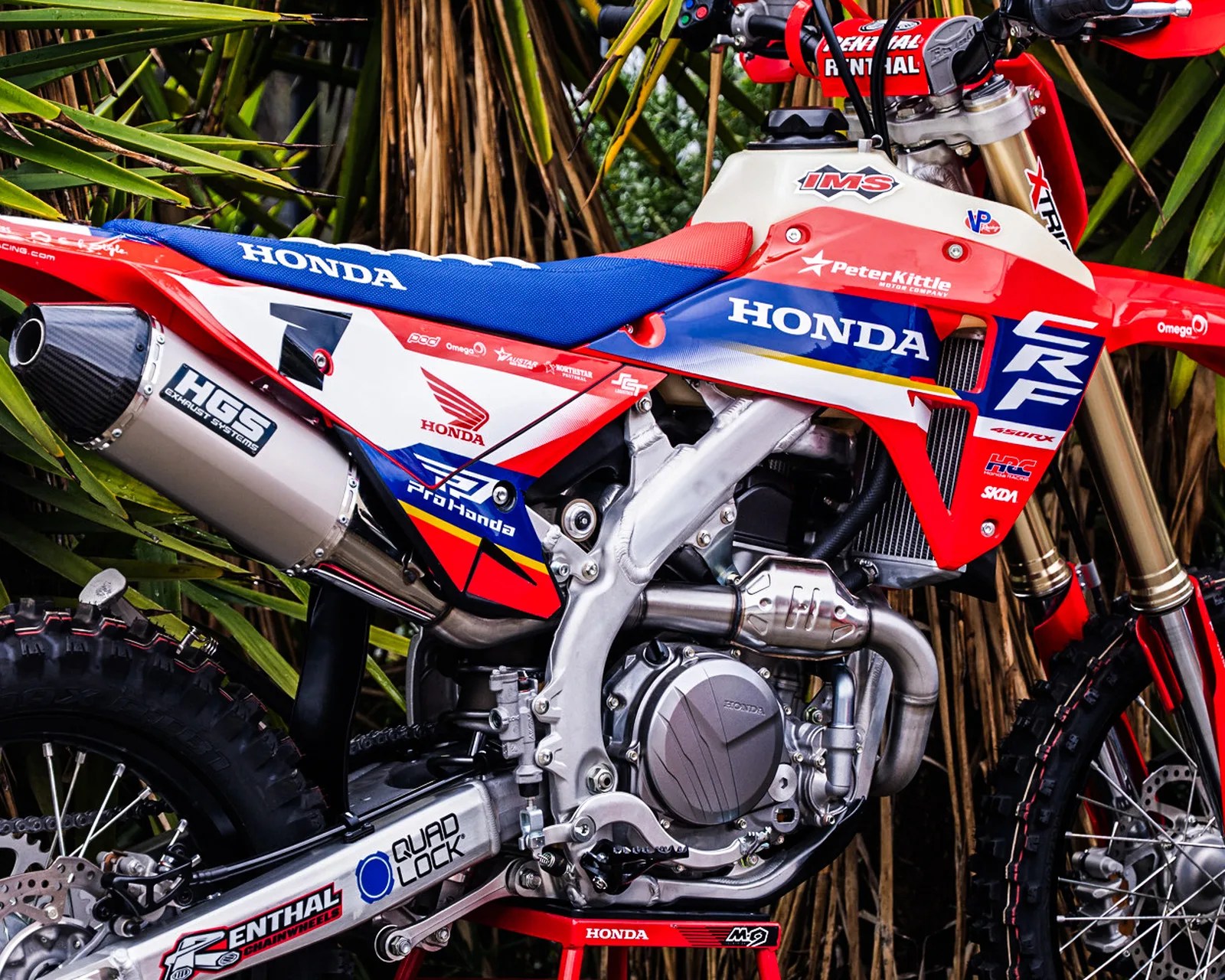 Red, white, and blue Honda CRF 450RX dirt bike with IMS fuel tank and HGS exhaust system, parked on a red stand.