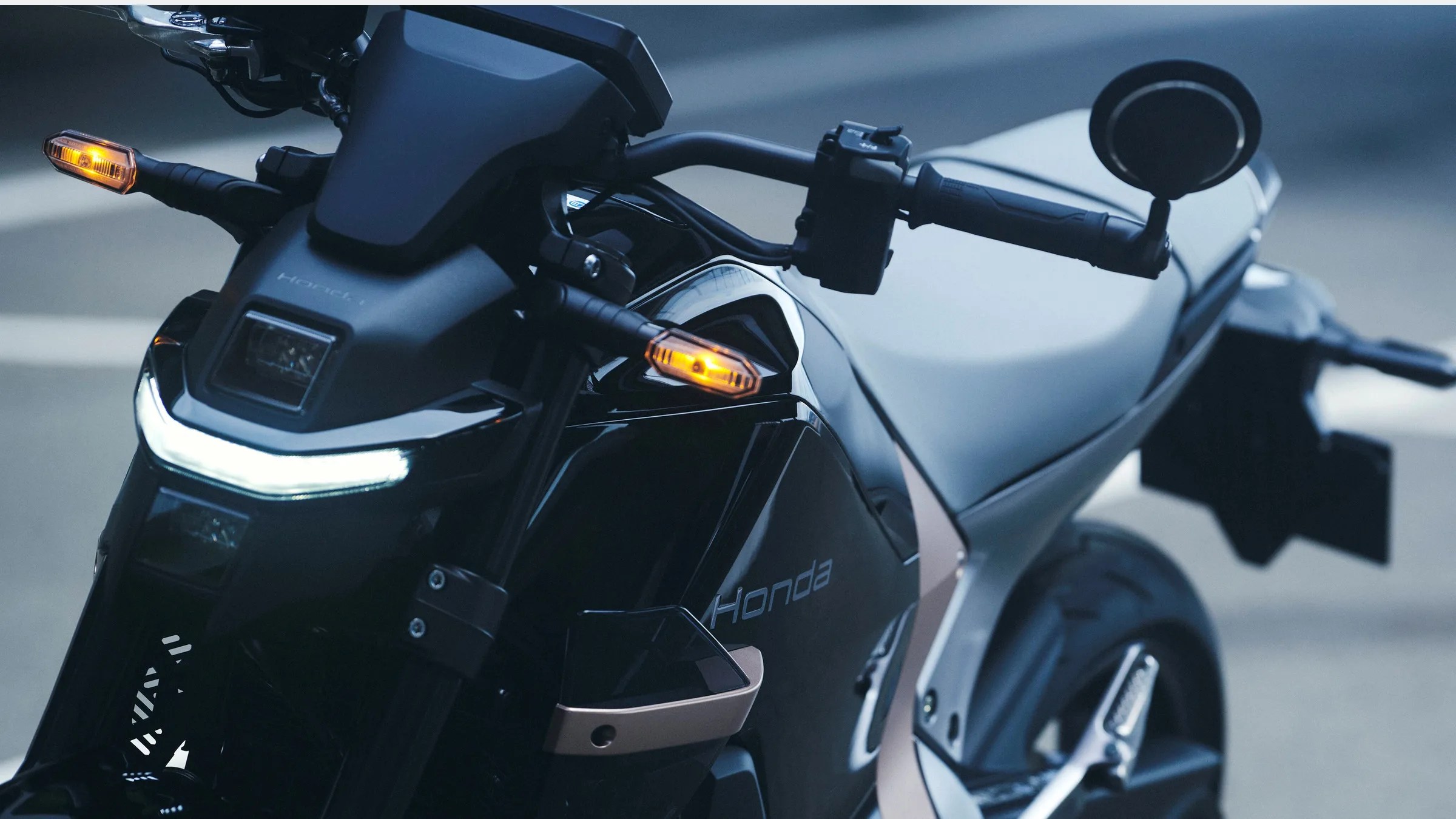 Close-up of a black and silver Honda motorcycle front with illuminated amber turn signals and white LED headlight strip.