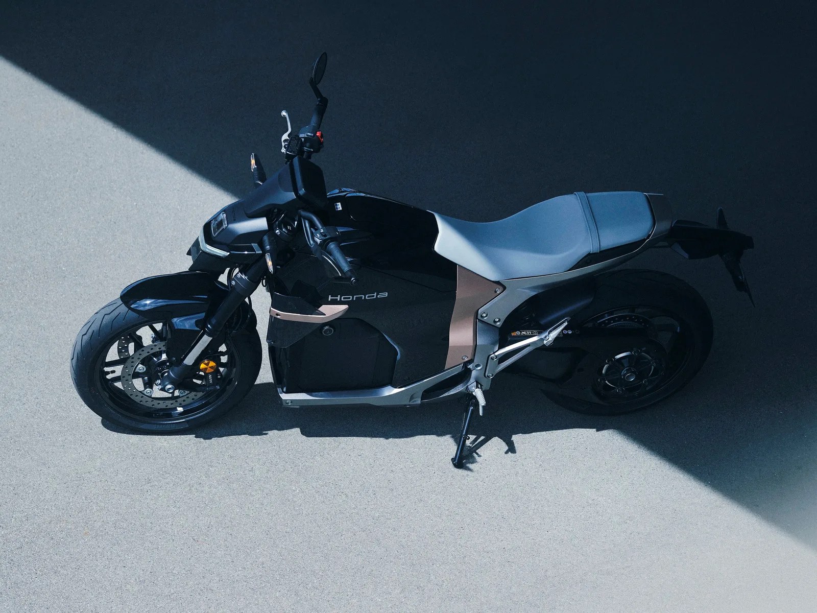 Black and silver Honda electric motorcycle parked on a concrete surface with a shadow diagonally across.