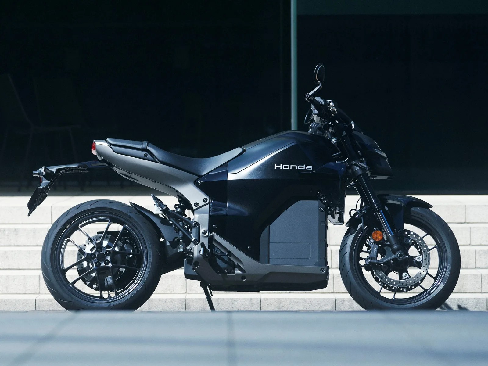 Sleek black Honda electric motorcycle with silver frame and disc brakes parked on pavement.
