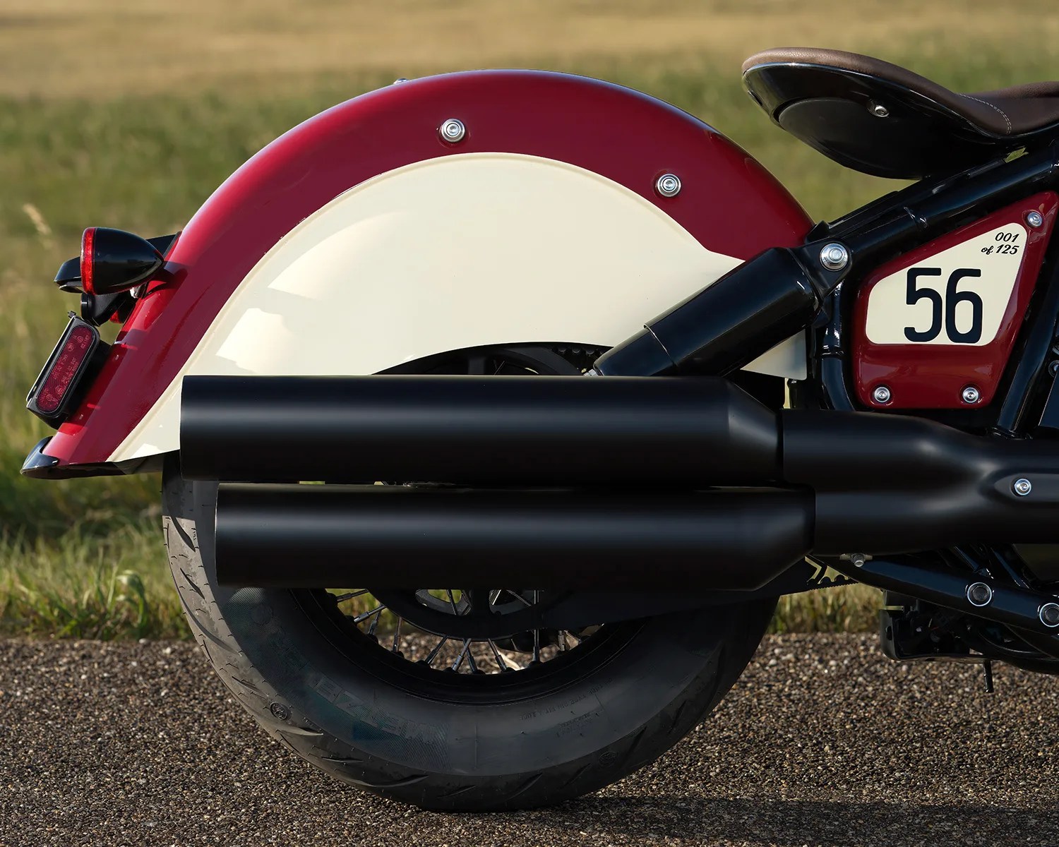 Rear wheel and dual black exhaust pipes of a red and cream motorcycle with the number 56 on the side panel.
