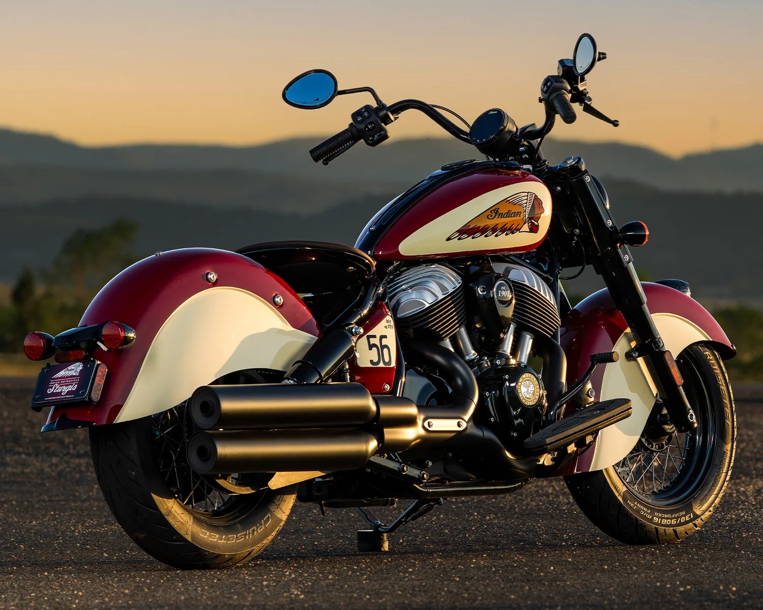 Red and cream Indian motorcycle with black exhaust pipes parked on asphalt at sunset.