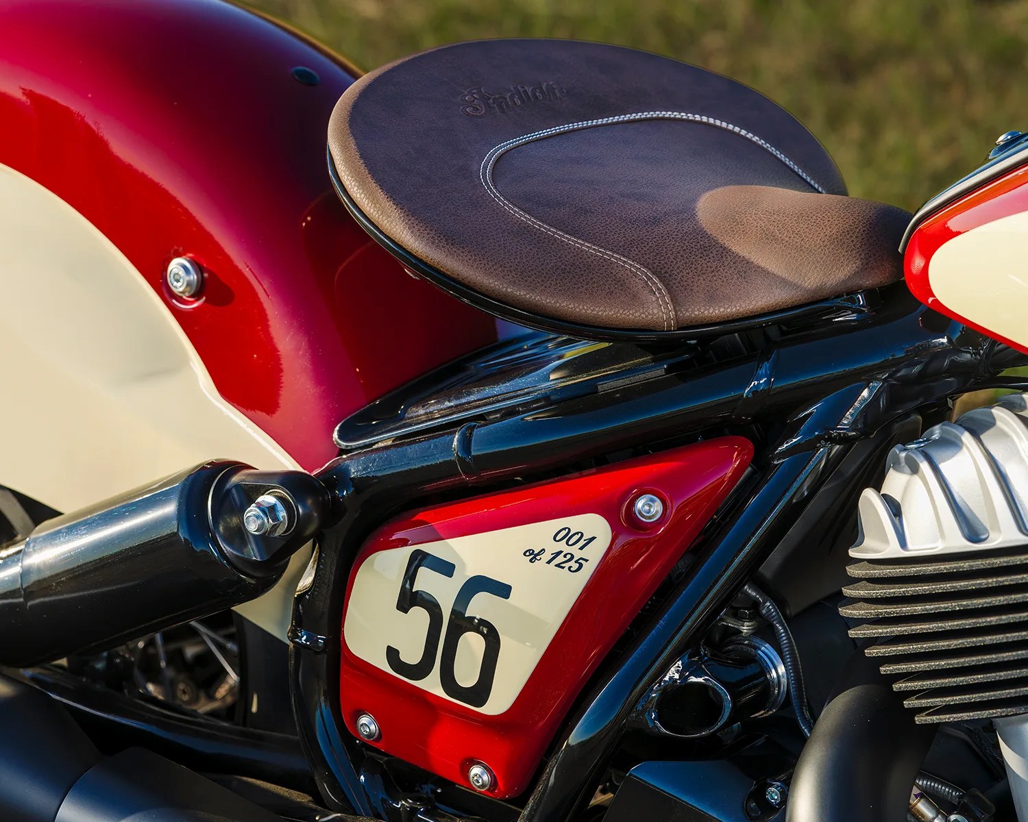 Close-up of a brown leather motorcycle seat with "Stadion" embossed, red and cream side panel numbered 56, and black frame.