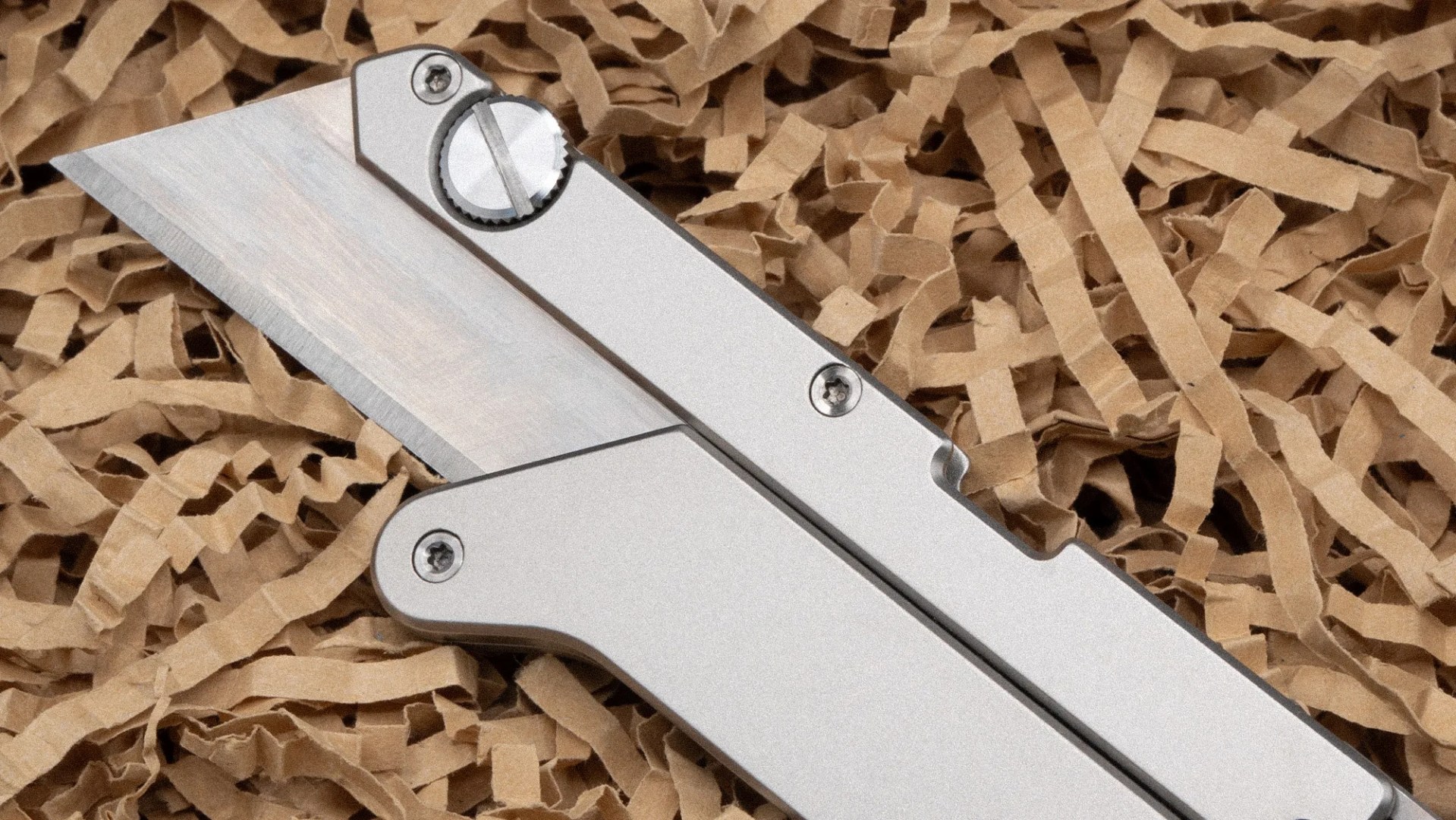 Silver metal folding knife with a sharp blade resting on shredded brown paper.