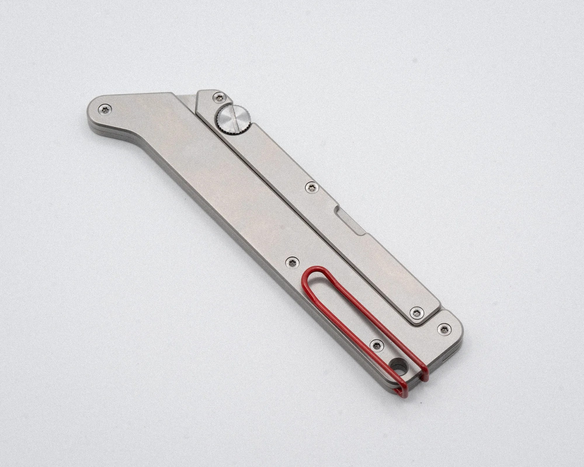 Silver metal folding knife with a red clip on a light gray surface.