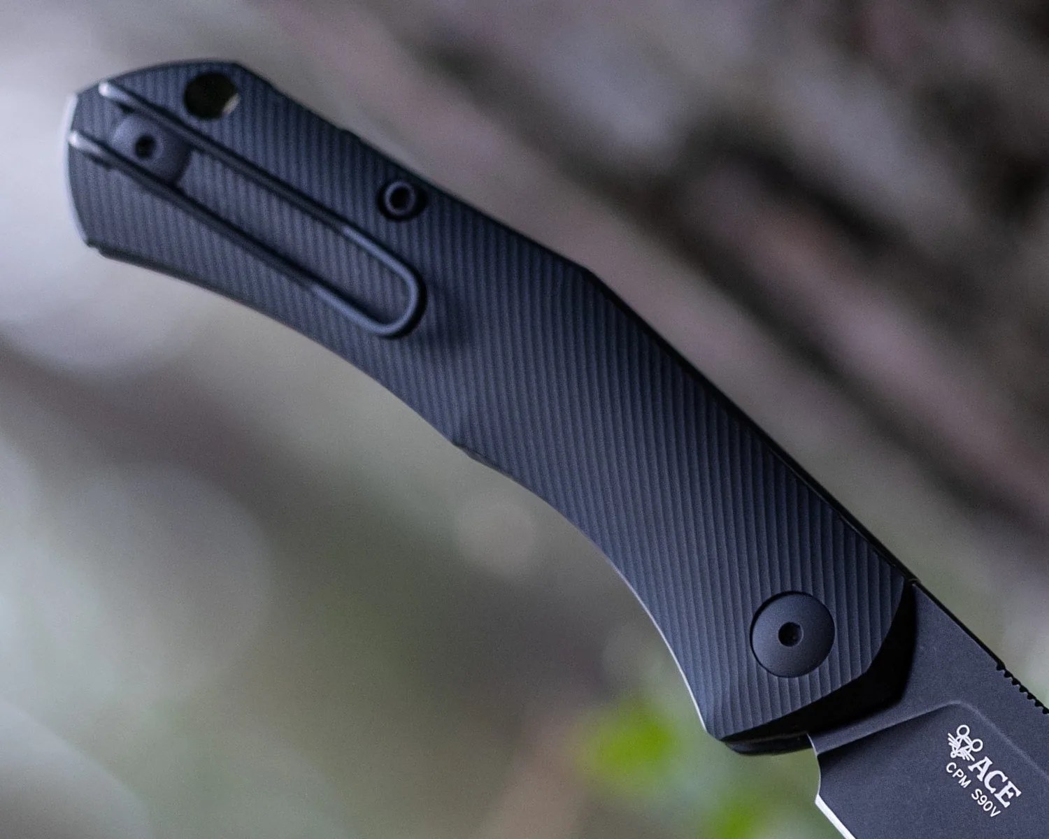 Black textured handle of a folding knife with a pocket clip and visible screws.